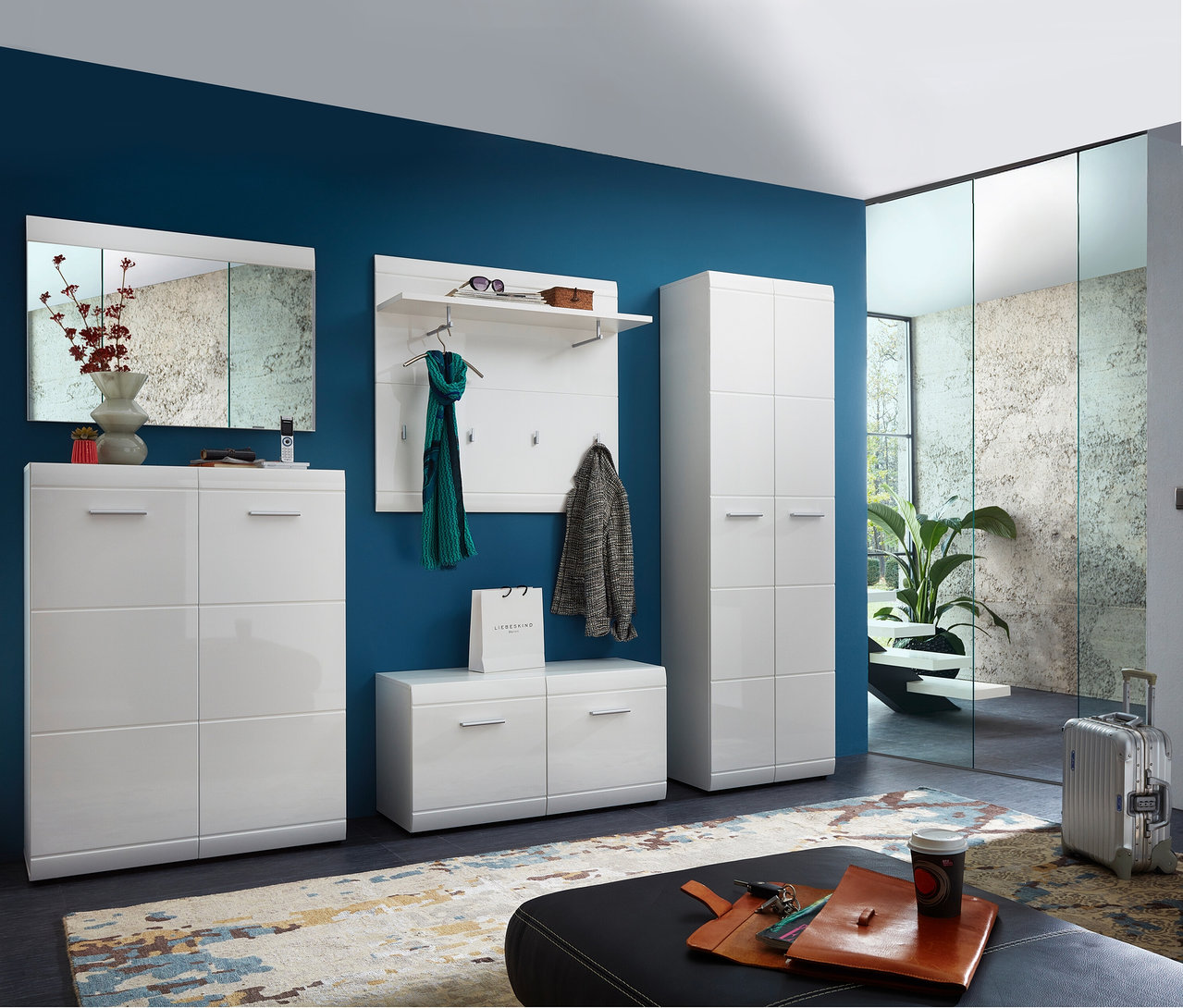 Eingangsbereich mit weißem »ADANA« Garderobenschrank, Schuhschrank, Bank und Spiegel an einer blau gestrichenen Wand.