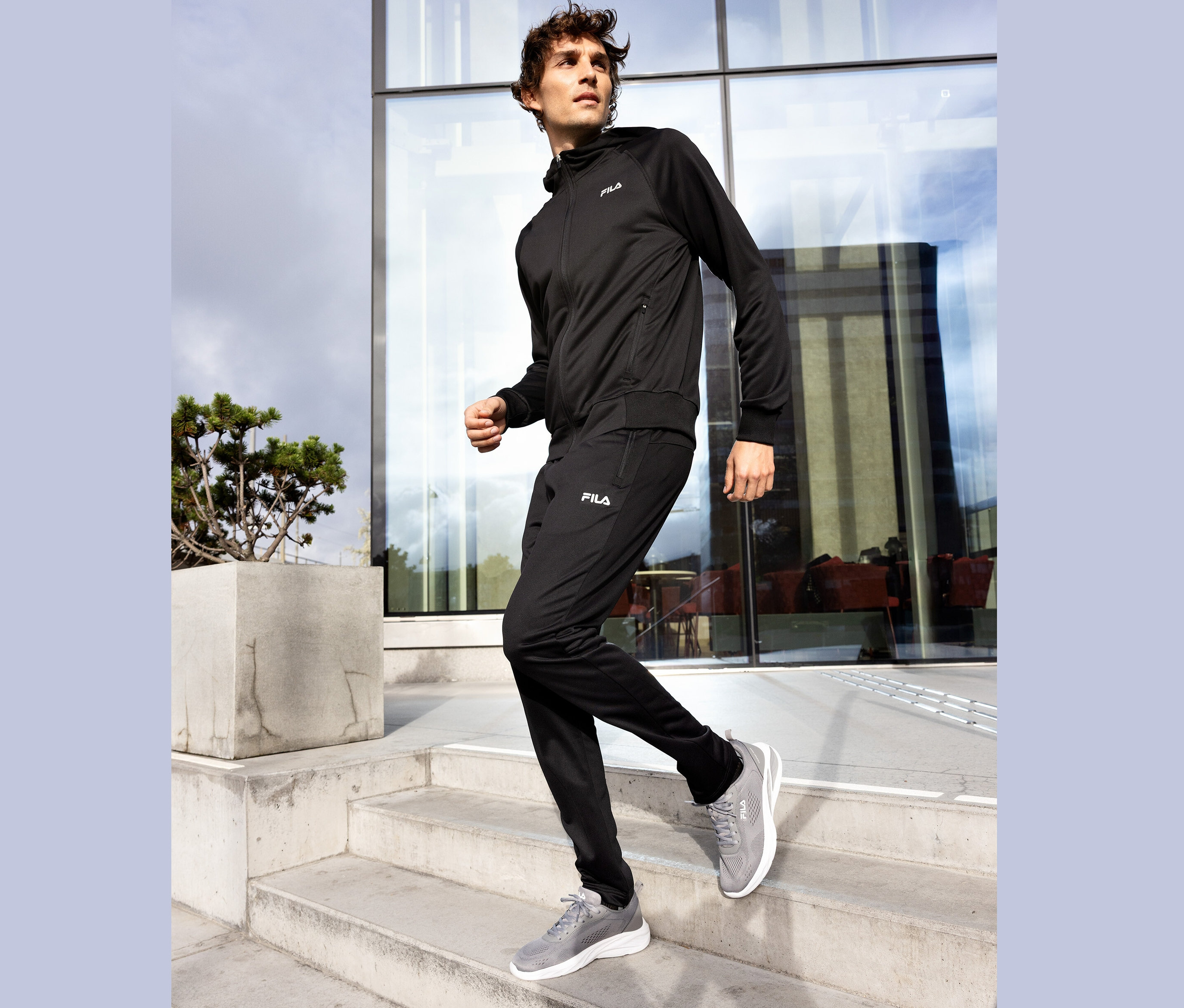 Mann in schwarzem Fila Trainingsanzug und grauen Turnschuhen geht eine Betontreppe hinunter.
