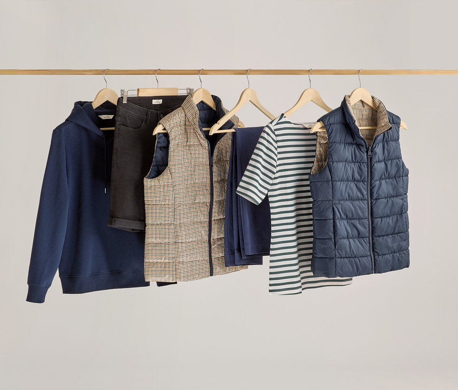 Kleidung hängt an einer Holzstange, darunter ein grünes, gestreiftes Halbarmshirt.