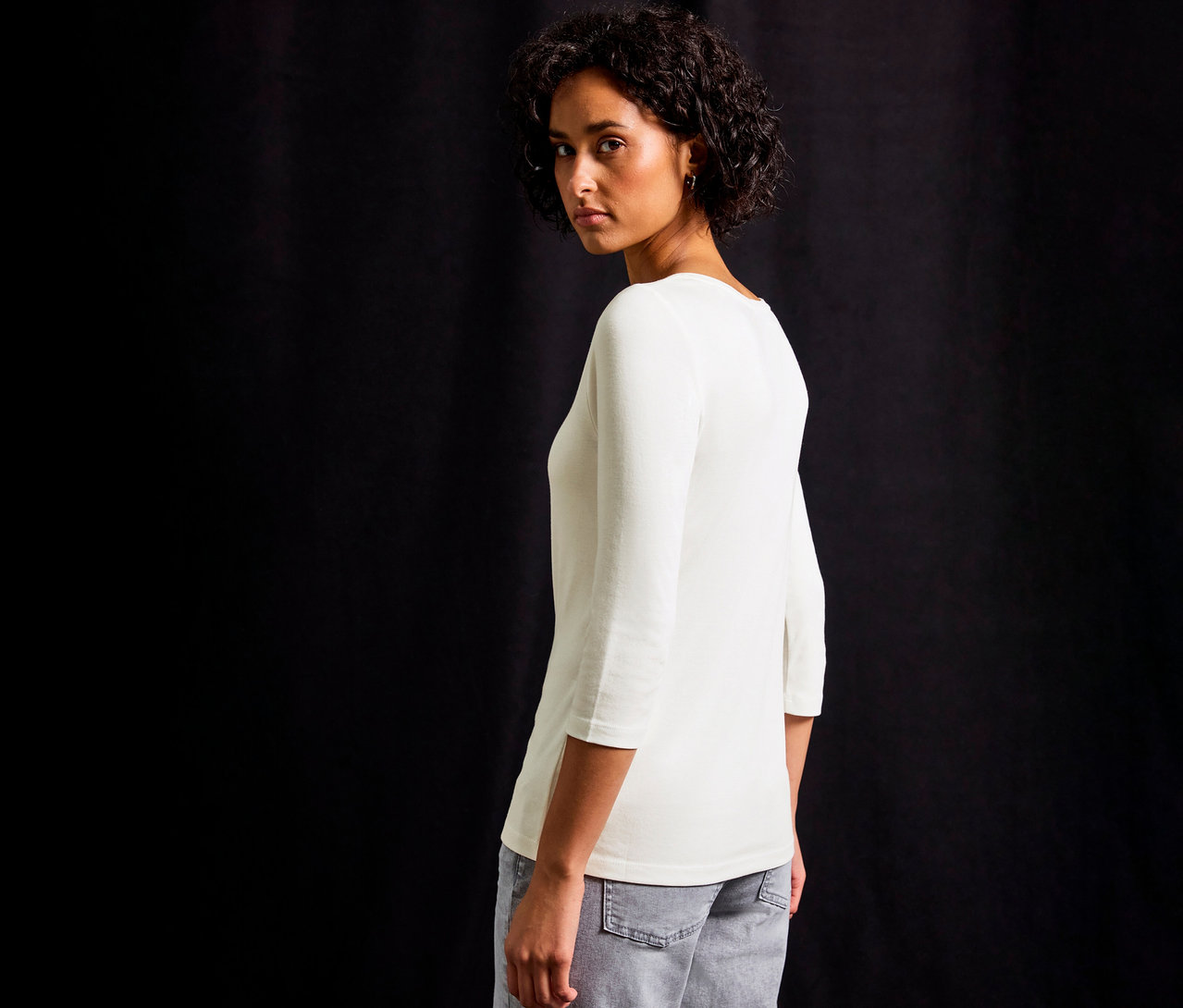 Frau blickt über ihre Schulter und trägt ein weißes Street One 3/4-Shirt mit Knopfdetail.