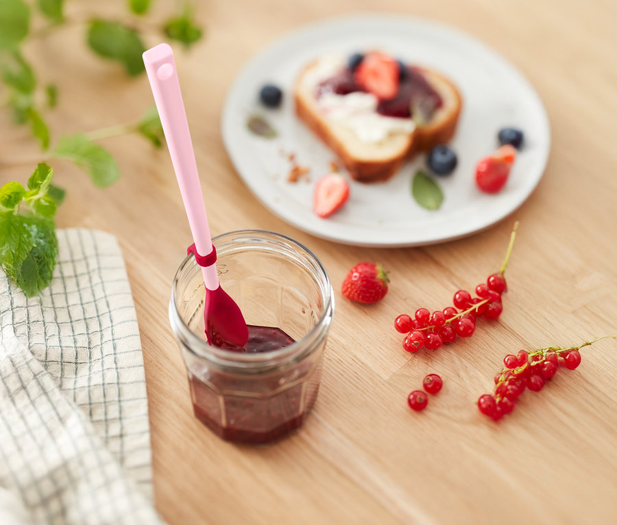 Marmeladenglas mit rosa Löffel, Toast mit Erdbeeren und Blaubeeren und Johannisbeeren auf einem Holztisch.