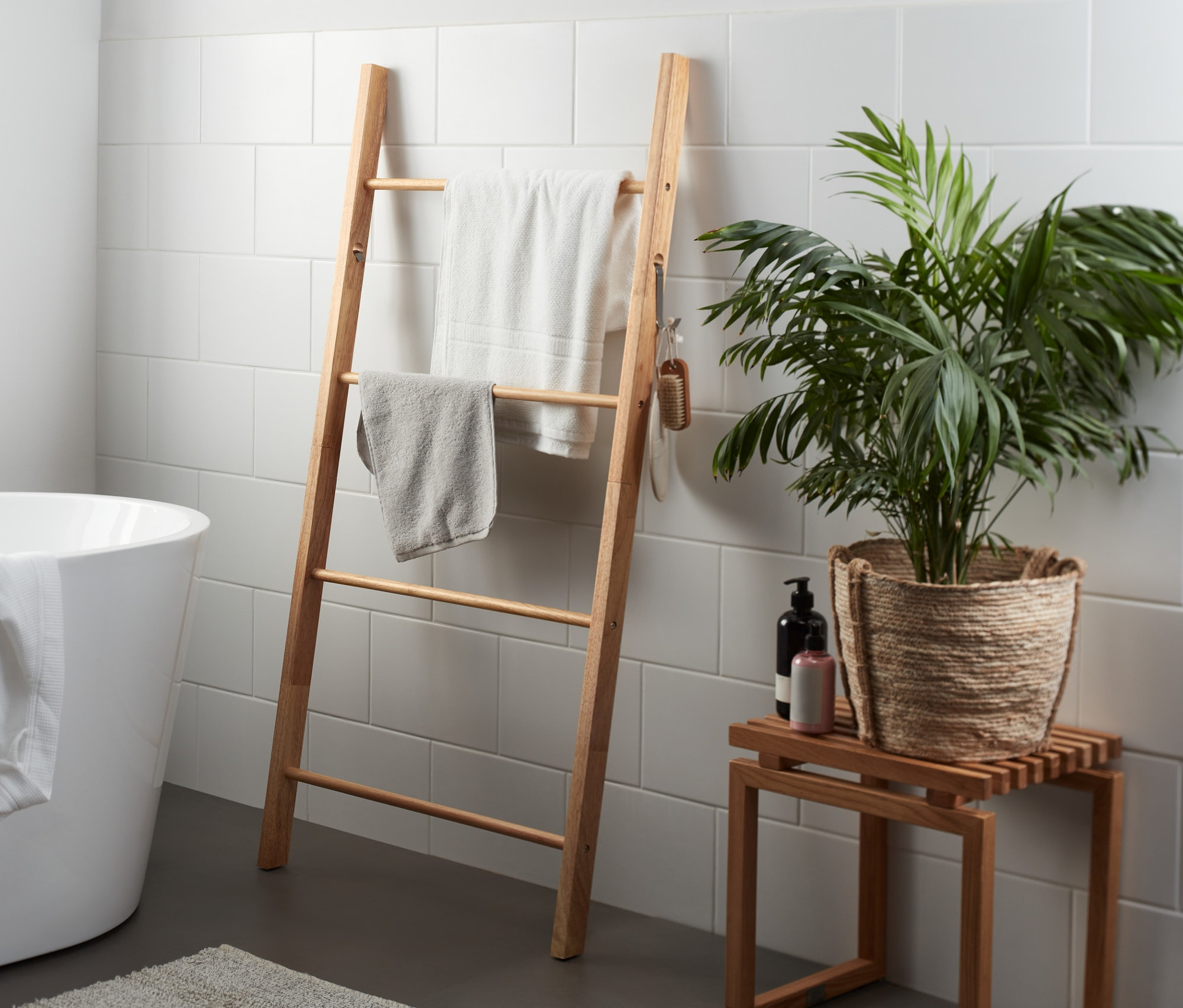 Im Badezimmer stehen eine extra breite Handtuchleiter mit zwei Handtüchern, eine Badewanne und ein Tisch mit einer Pflanze.