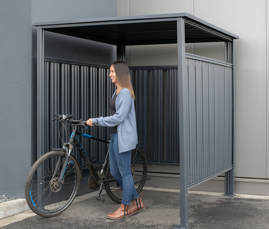 Frau schiebt Fahrrad in einen Fahrradunterstand.