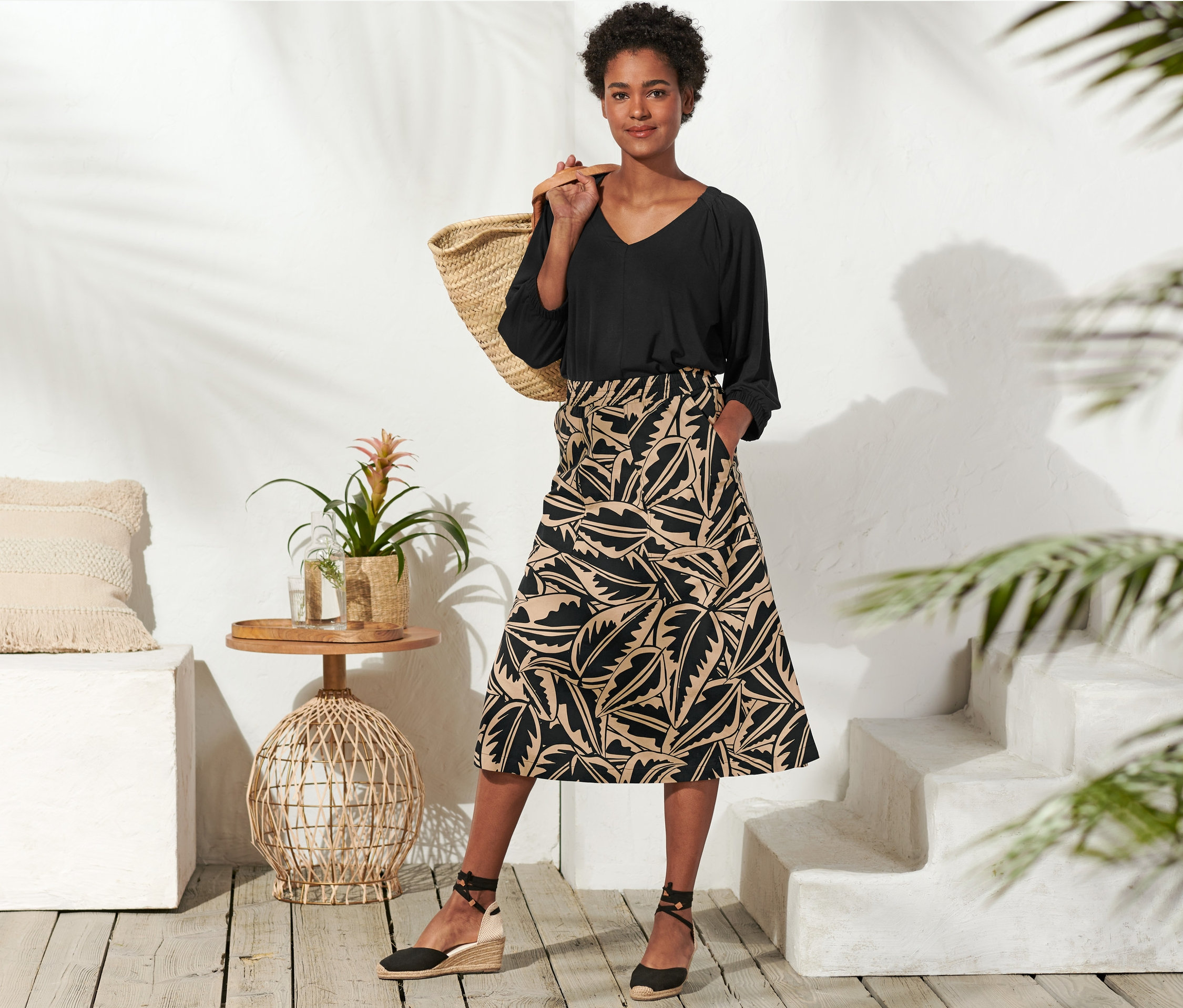 Frau posiert in schwarzem Oberteil und Popeline-Rock mit Alloverprint. Eine Tasche hängt über ihrer Schulter.