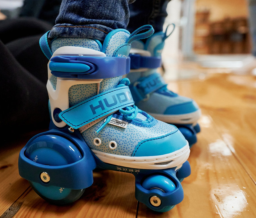 Nahaufnahme von Kinderfüßen in blauen HUDORA Rollschuhen "My First Quad" auf einem Holzboden.