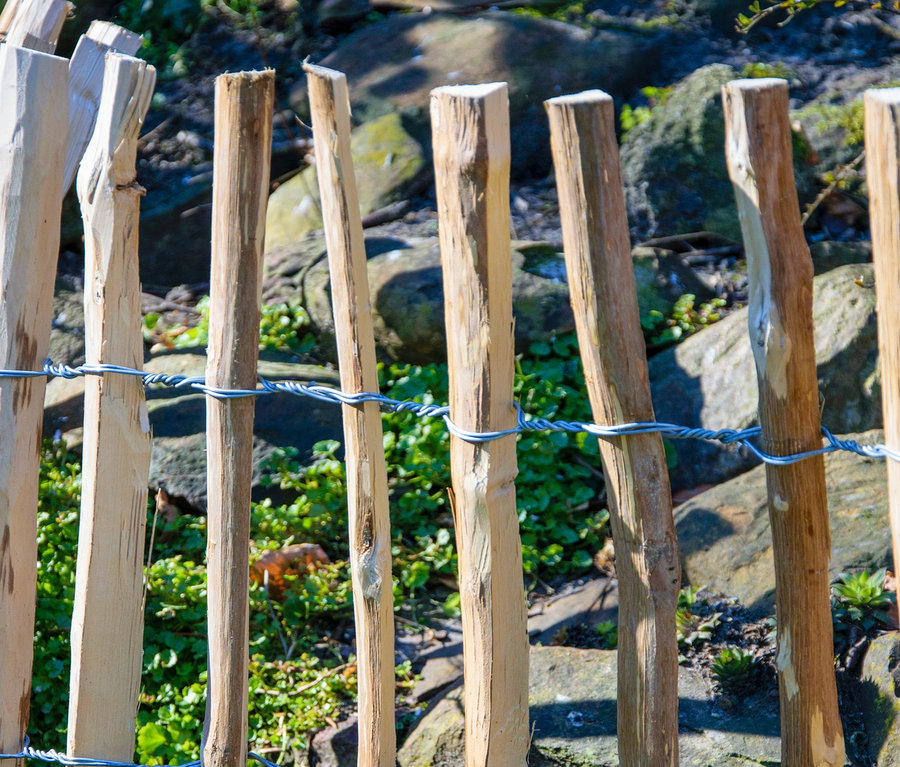 Holzzaun mit Drahtgeflecht im Hintergrund mit Steinen und Grün. Dobar Rankgitter-Spalier.