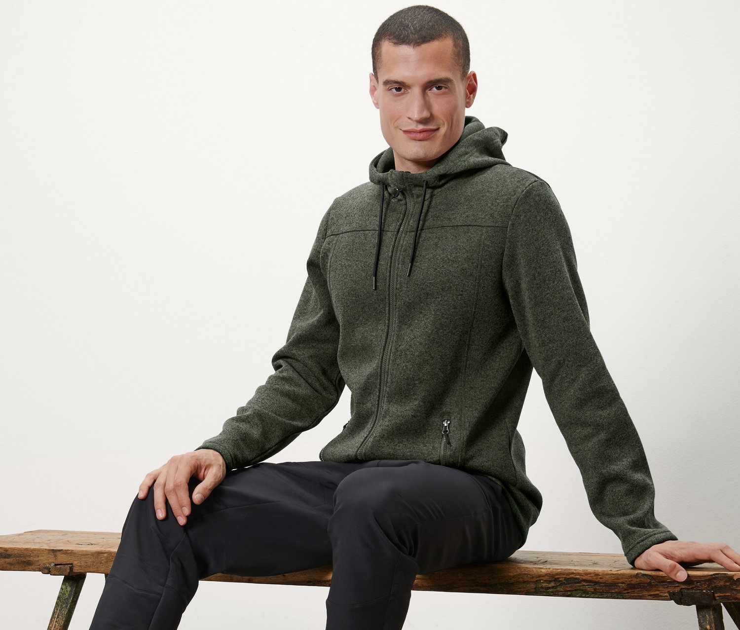 Mann sitzt auf einer Bank und trägt eine Strickfleece-Jacke.