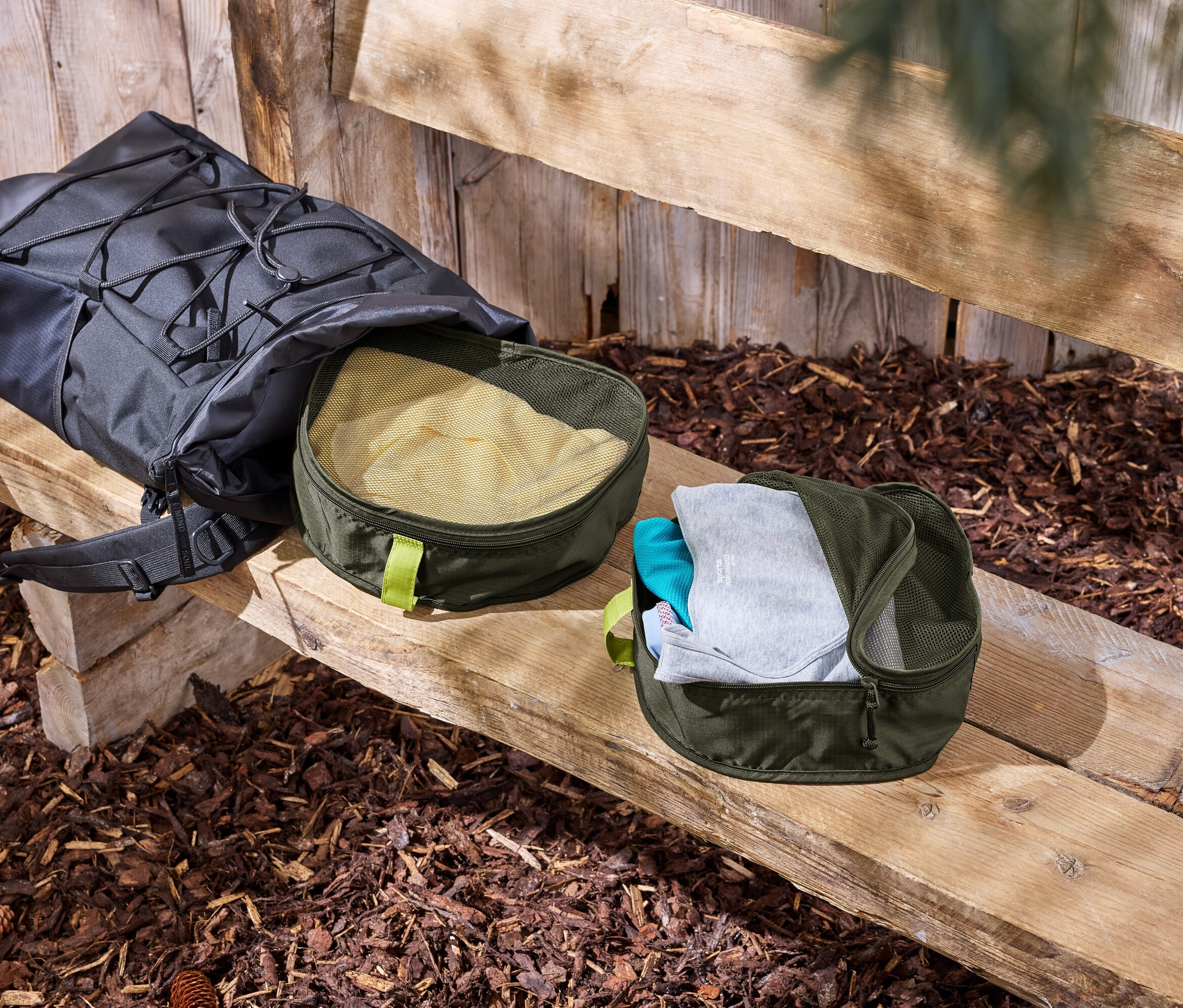 Schwarzer Rucksack liegt auf einer Holzbank neben zwei grünen Kleider-Organizer.