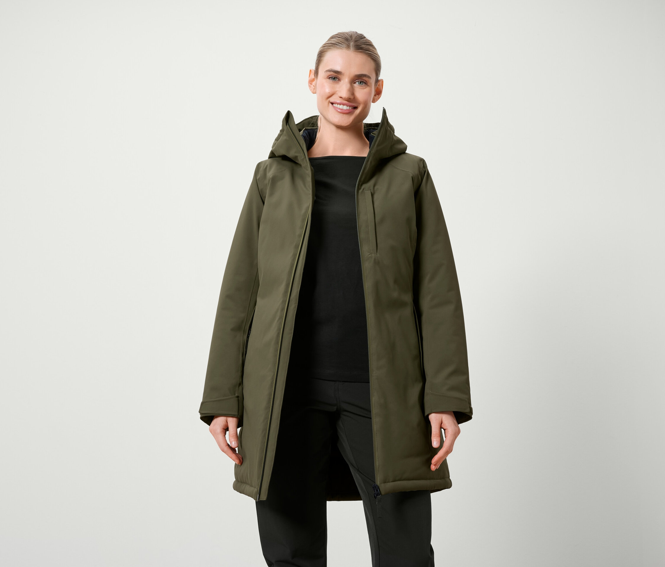 Frau posiert in olivgrüner Jacke mit Kapuze und schwarzer Kleidung.