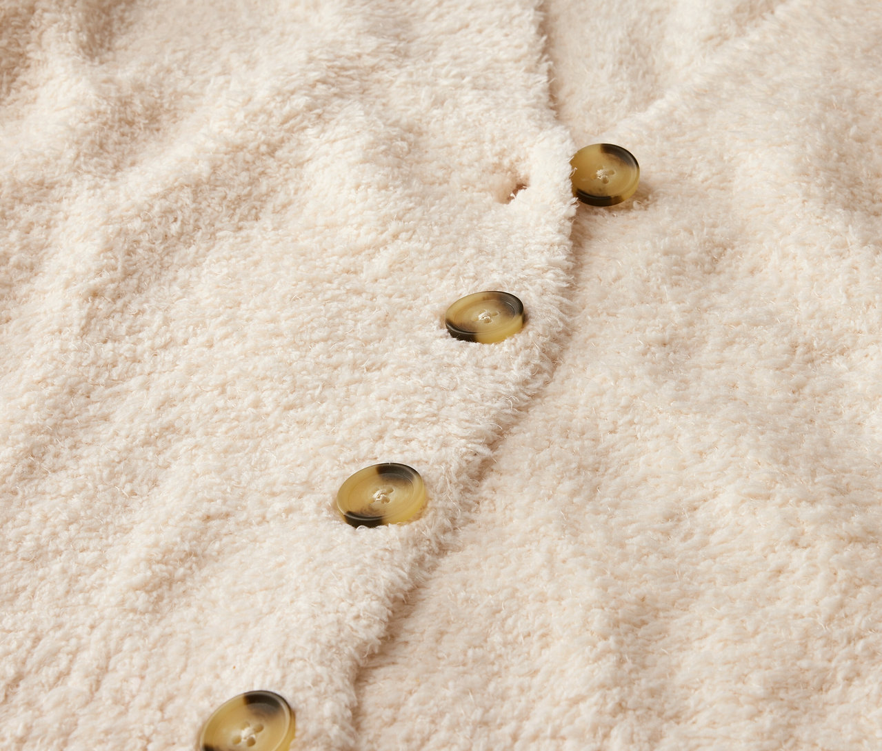 Detailaufnahme einer beige Strickjacke mit Knöpfen.