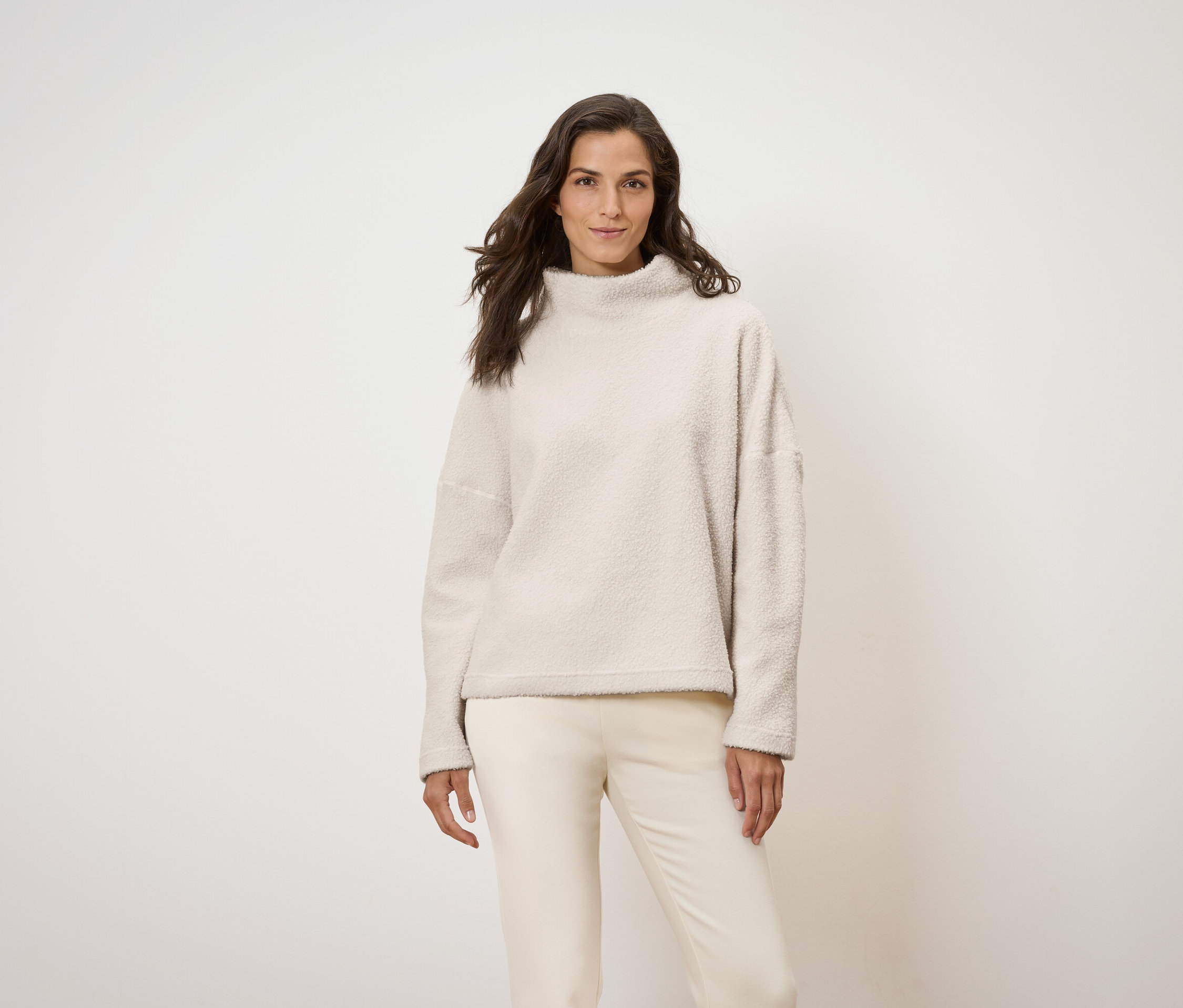 Frau posiert in cremefarbenem Pullover und Hose.