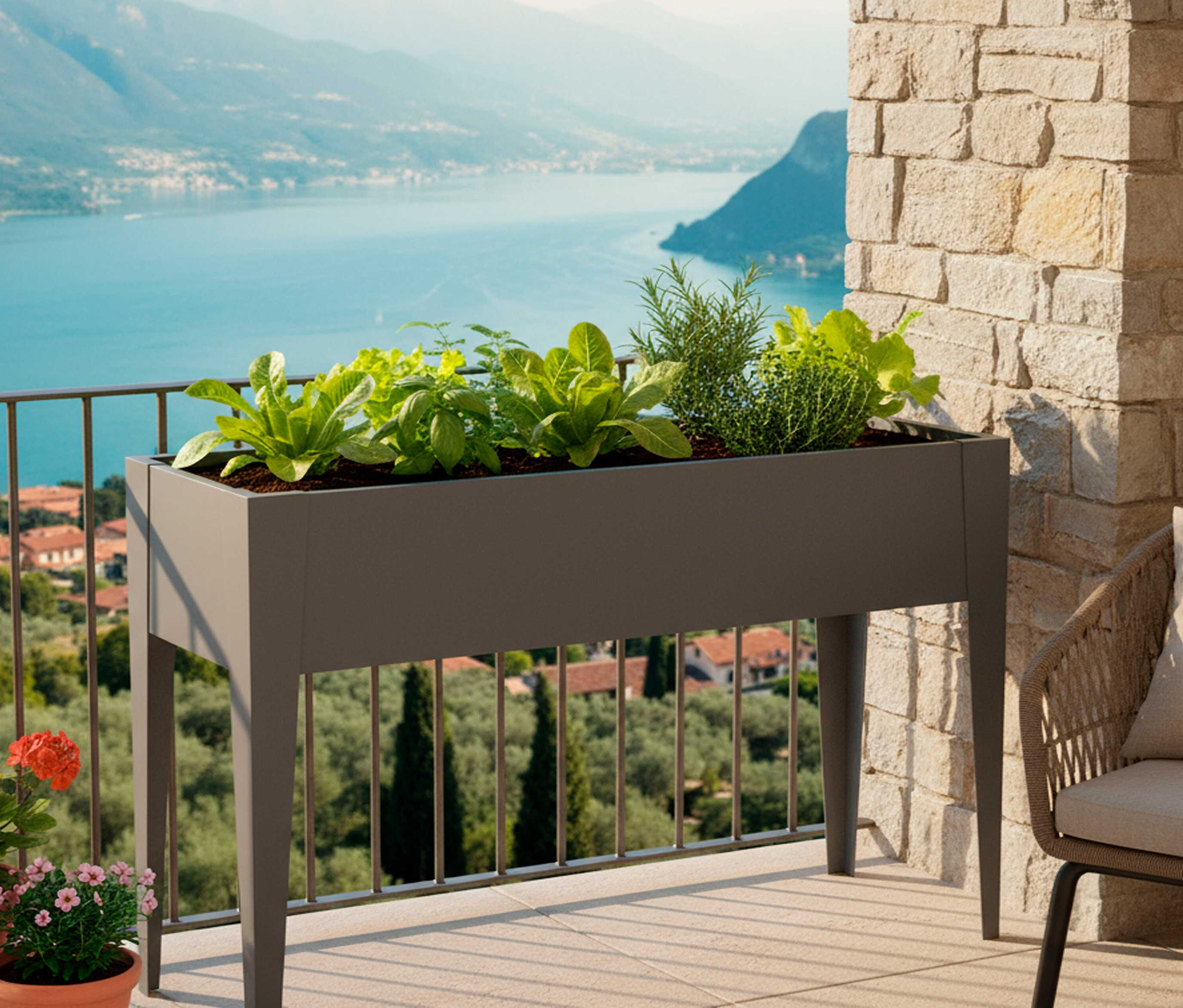 Ein erhöhtes, rechteckiges Pflanzgefäß mit Salat und Kräutern steht auf einem Balkon mit Blick auf einen See.