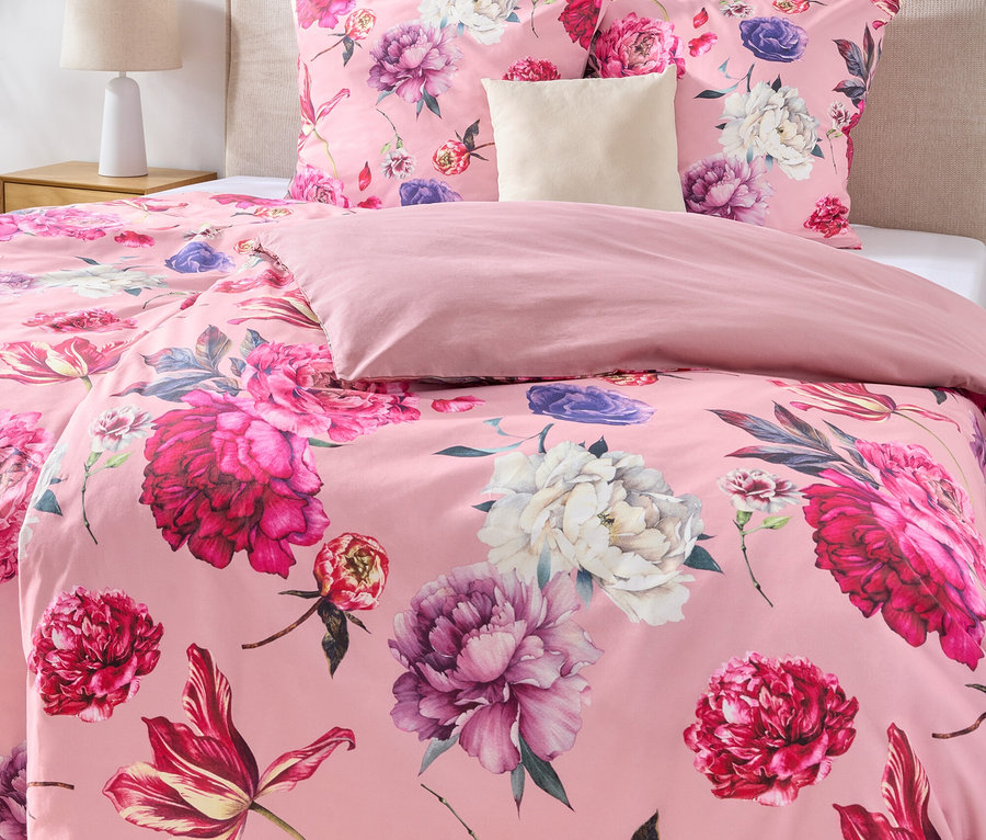 Nahaufnahme eines Bettes mit rosa Bettwäsche mit Blumenmuster, einem beigen Kopfteil und zwei gerahmten Bildern an der Wand.