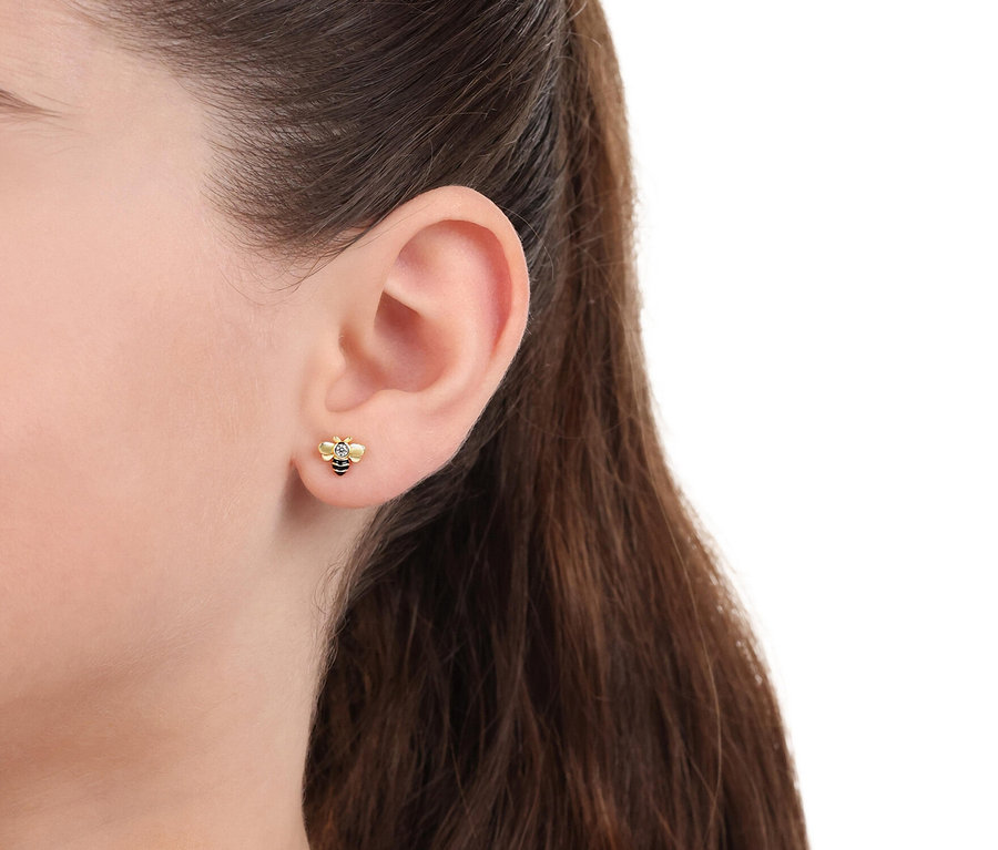 Nahaufnahme eines Ohrläppchens mit einem einzelnen Ohrstecker in Form einer Biene mit einem kleinen Stein.