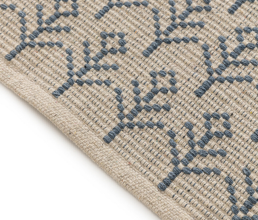 Detailaufnahme eines beigen Teppichs mit blauem floralem Muster.