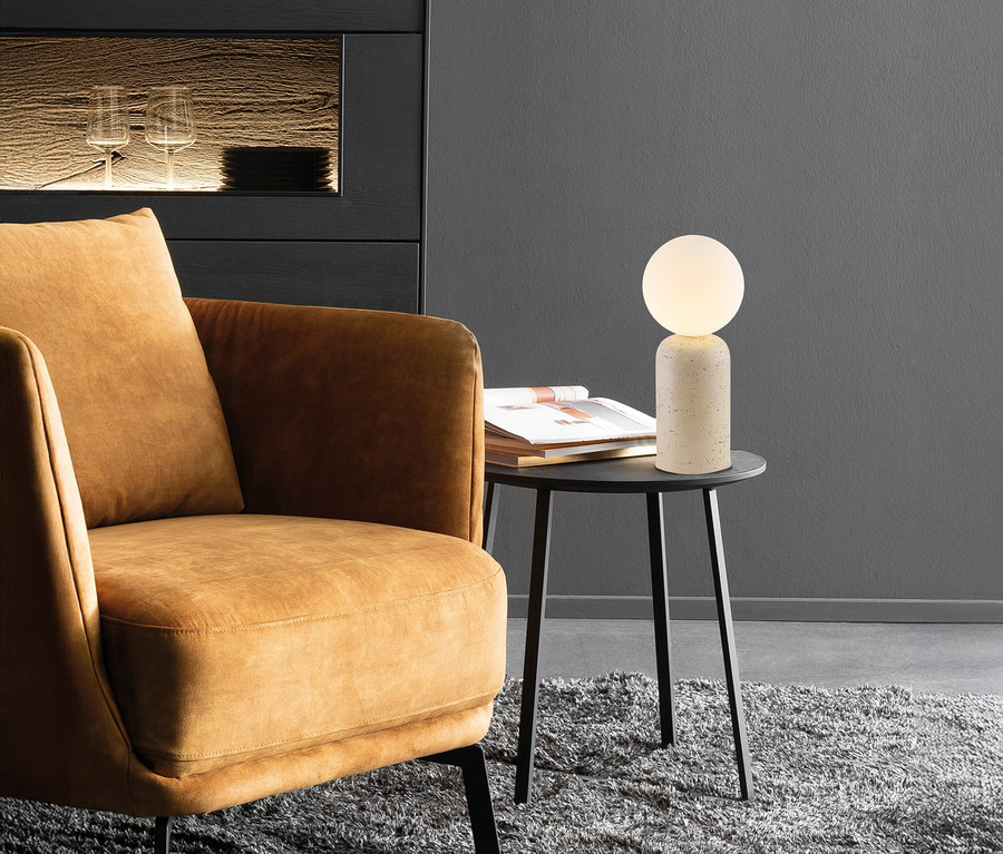 Brauner Sessel neben einem schwarzen Tisch mit der SCHÖNER WOHNEN-Kollektion Tischleuchte »Traventa« und einem Buch.
