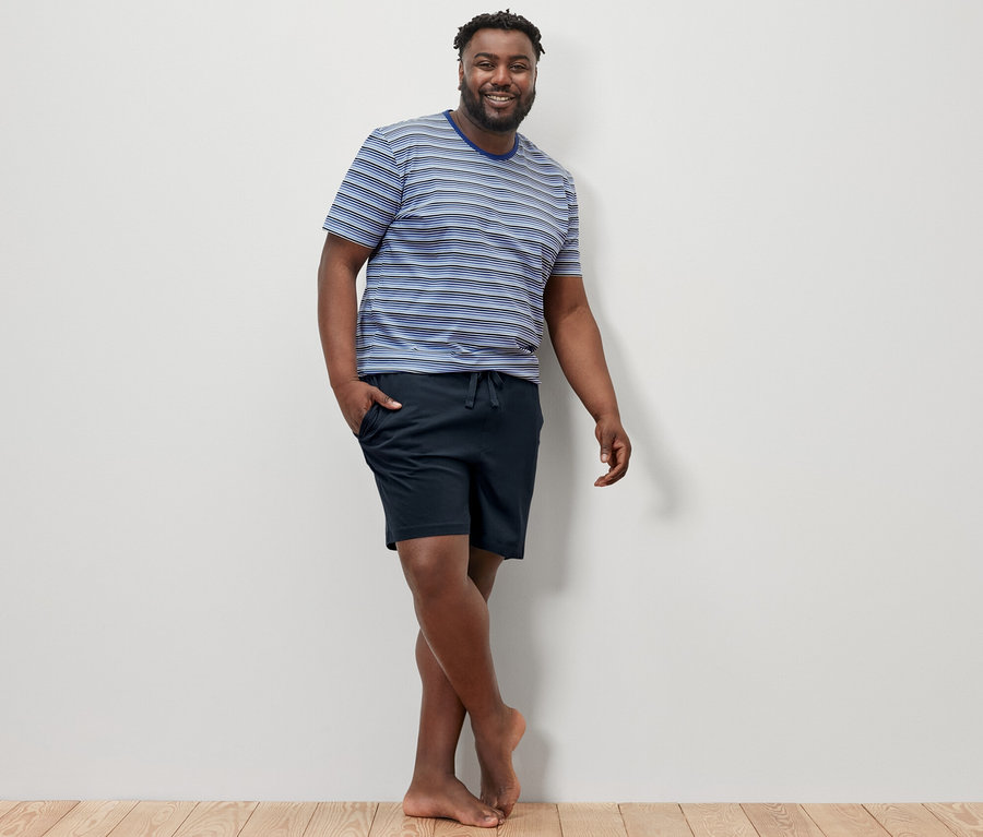 Mann posiert auf Holzboden und trägt einen blau-dunkelblauen Shorty-Pyjama.