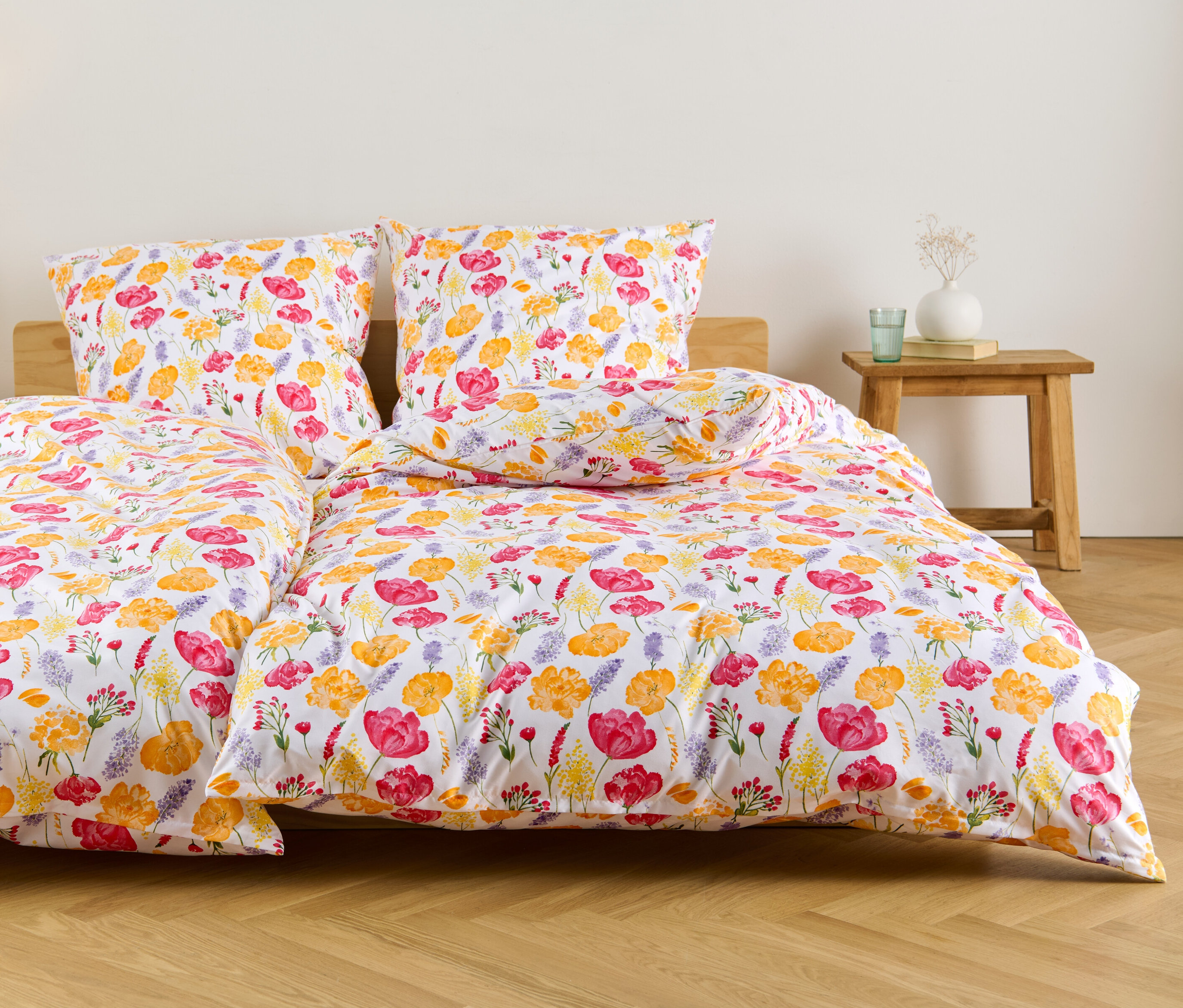 Weiße Microfaser-Bettwäsche in Normalgröße und Übergröße mit Blumenmuster liegt auf einem Bett.