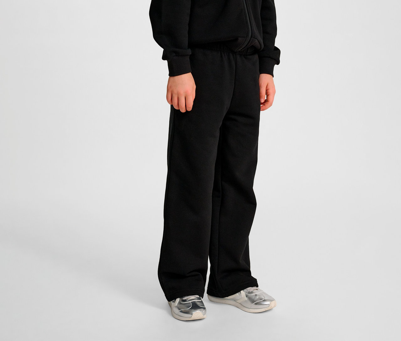 Junge trägt schwarze HUMMEL HMLJR Loose WL Sweatpants und silberne Schuhe.
