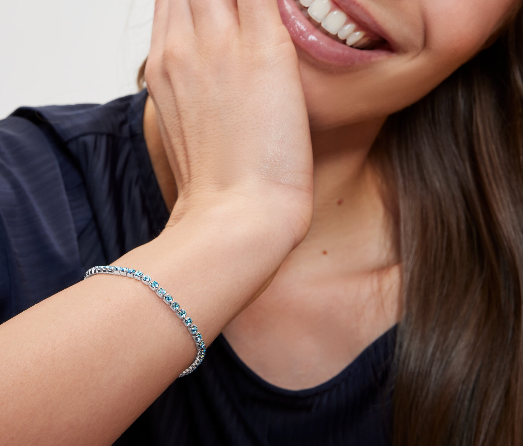 Lächelnde Frau berührt ihr Gesicht und trägt ein Tennisarmband mit Paperlinkkette.