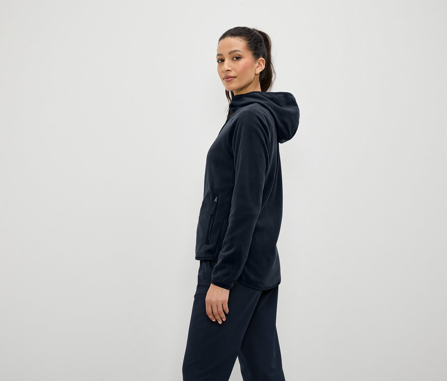 Frau trägt marineblauen Fleece-Hoodie und -Hose, steht seitlich.