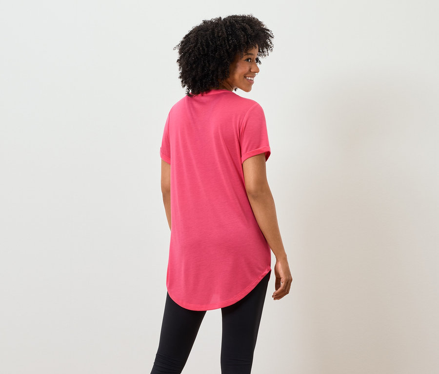 Von hinten ist eine Frau mit lockigem Haar in einem pinkfarbenen T-Shirt und schwarzen Leggings zu sehen.