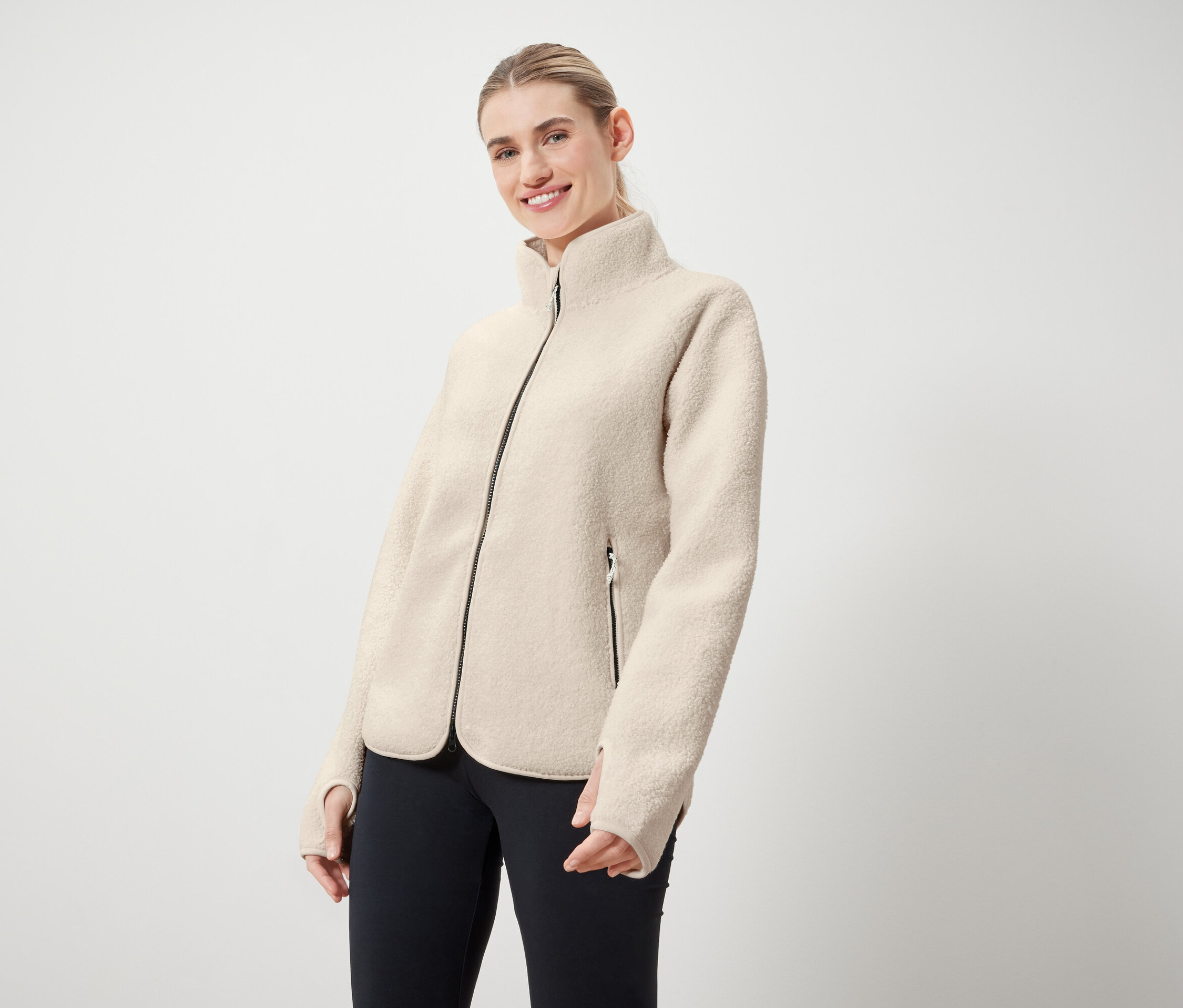 Frau trägt eine cremefarbene Jacke mit schwarzem Reißverschluss und schwarze Leggings.