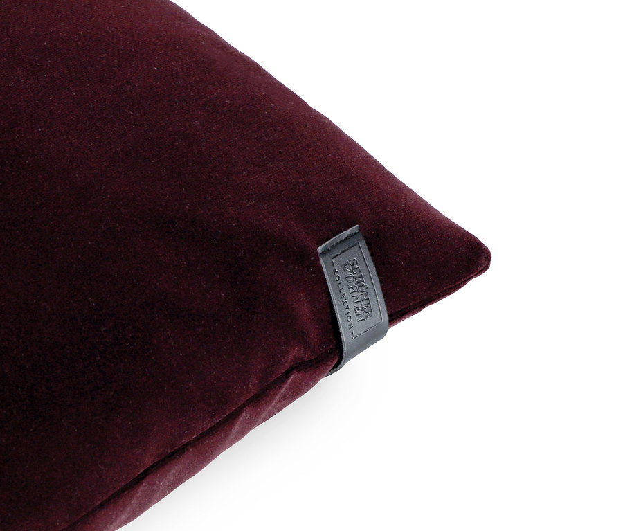 Ein weinrotes Dekokissen mit einem schwarzen Etikett in der unteren rechten Ecke.