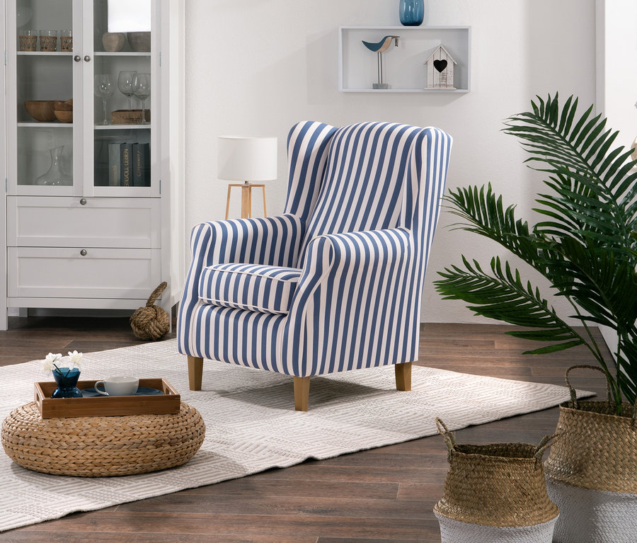 Ein Ohrensessel mit Streifen steht im Wohnzimmer neben einem Schrank und einer Pflanze.