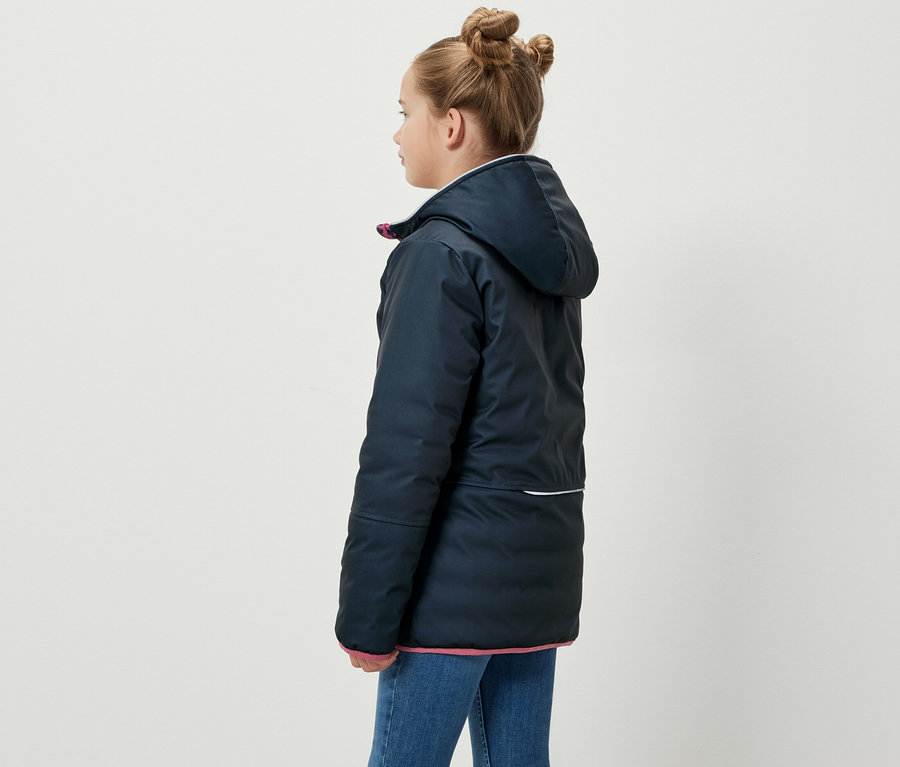 Mädchen steht seitlich und trägt eine blaue 2-in-1-Kinder-Softshell- und Steppjacke.