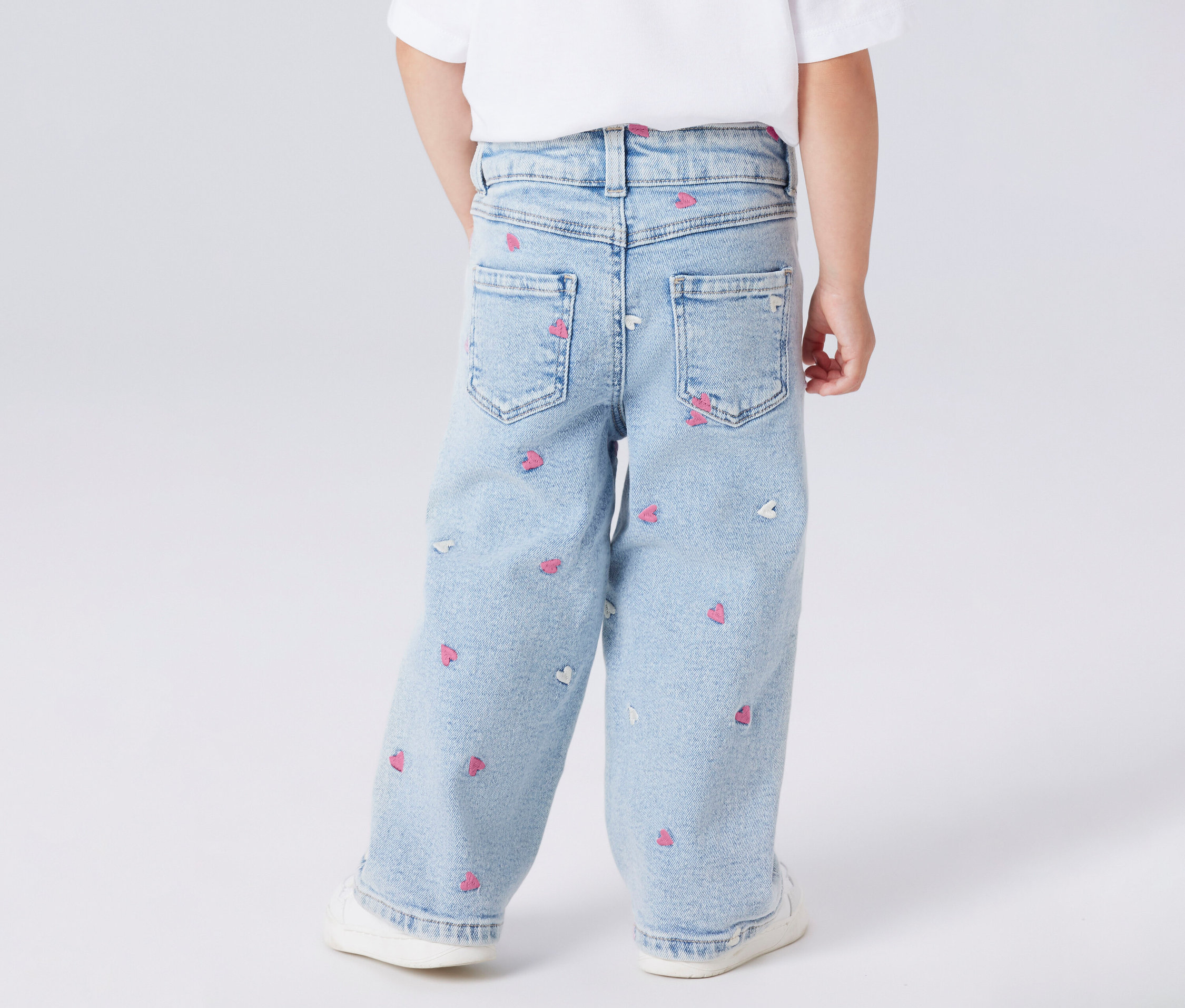 Rückansicht eines Kindes mit hellblauen Jeans mit rosa und weißen Herzaufdrucken.
