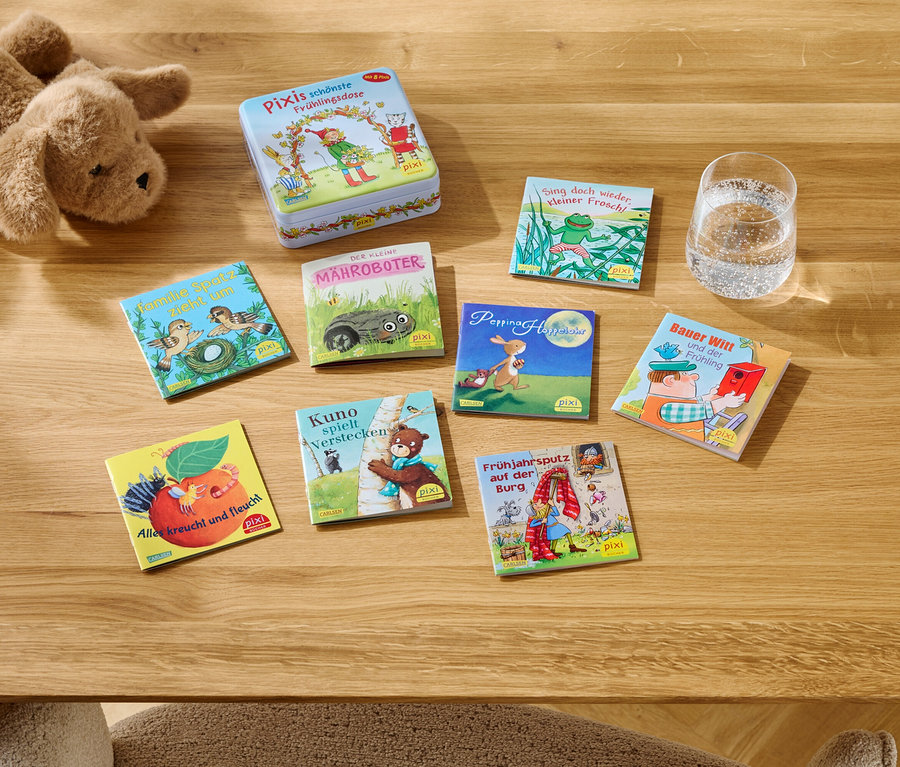 Auf einem Holztisch liegen ein Stofftier, eine Dose und mehrere Pixi-Bücher neben einem Glas Wasser.