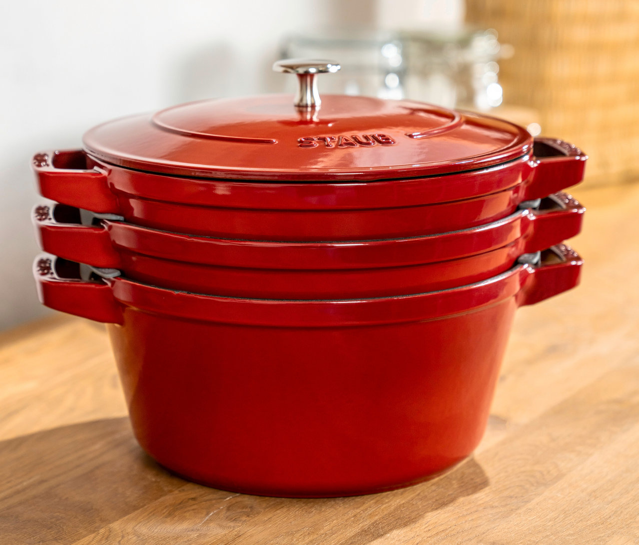 Gestapeltes, dreiteiliges STAUB Kochtopf-Set »La Cocotte« in Rot auf einem Holztisch.