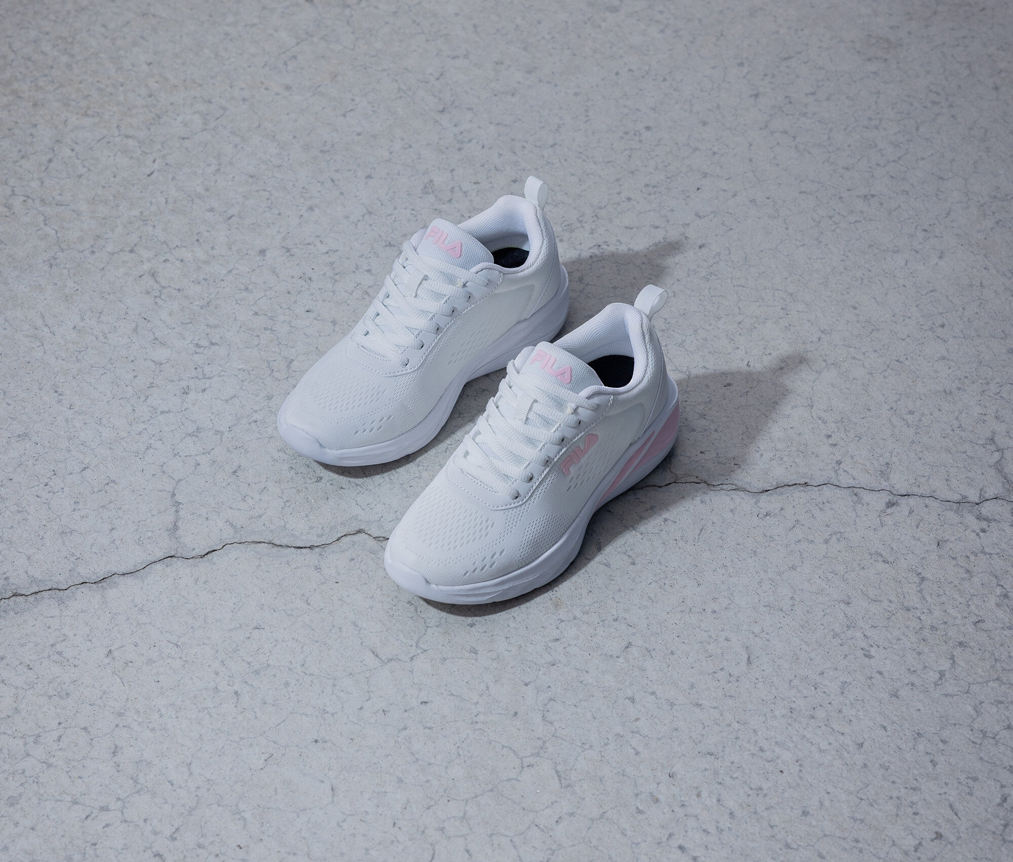Zwei weiße Fila-Sneaker mit pinkfarbenem Logo liegen auf einem grauen Untergrund.