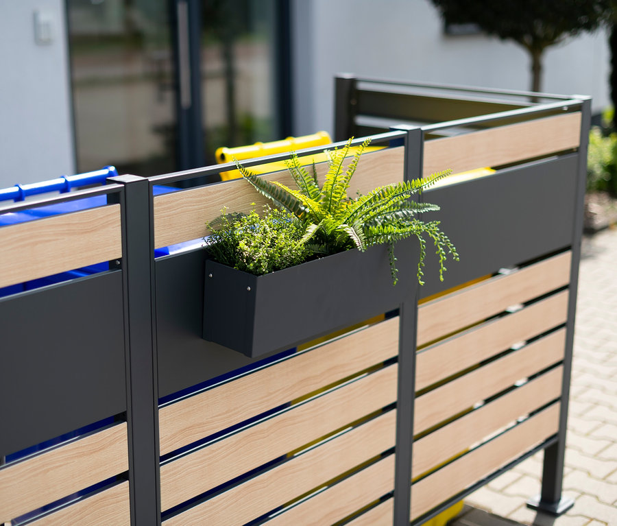 Grauer Stahl-Blumenkasten mit Pflanzen an einem Zaun befestigt.