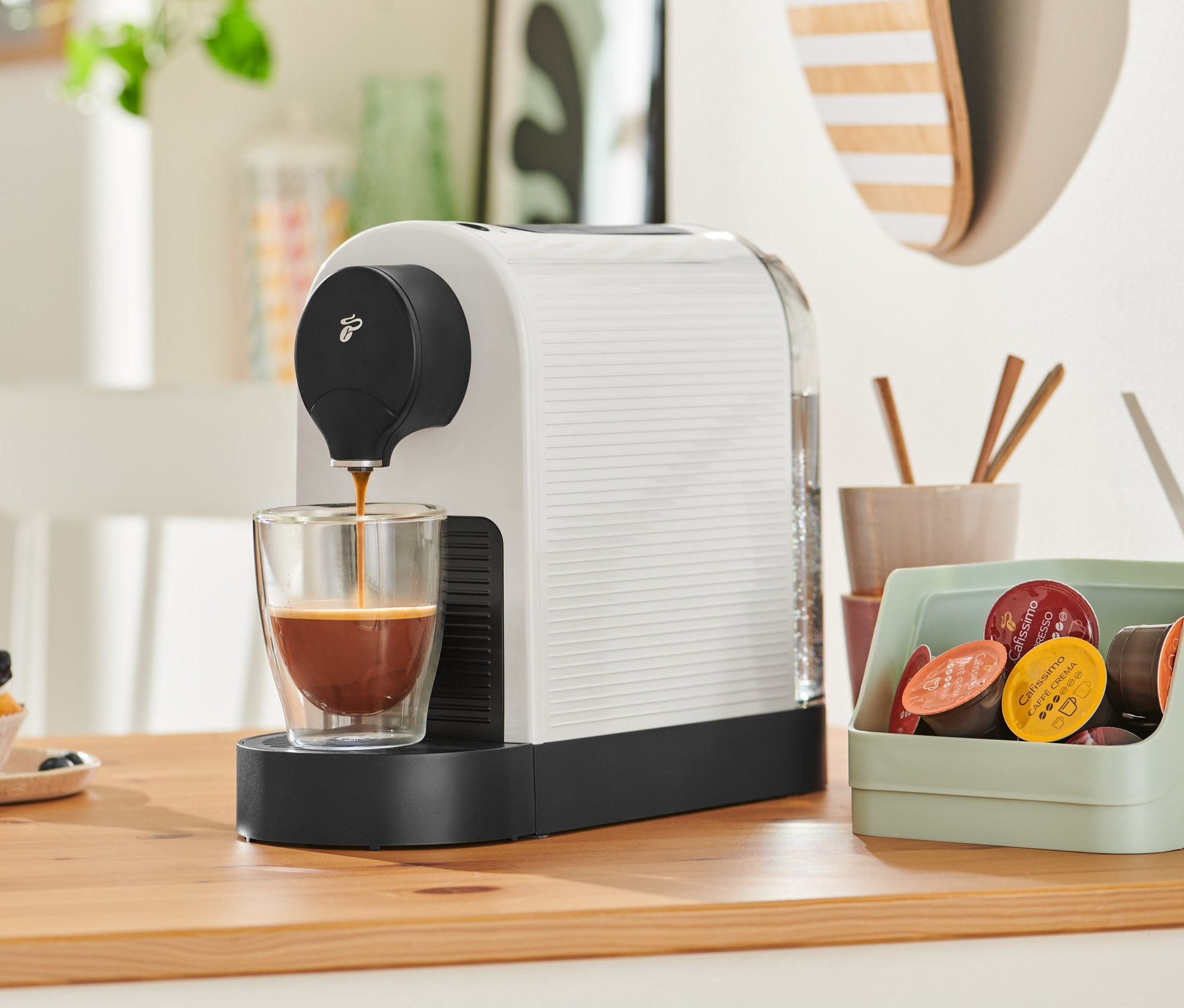 Cafissimo pure+, white Kaffeemaschine füllt Kaffee in ein Glas. Im Hintergrund befindet sich ein Muffin.