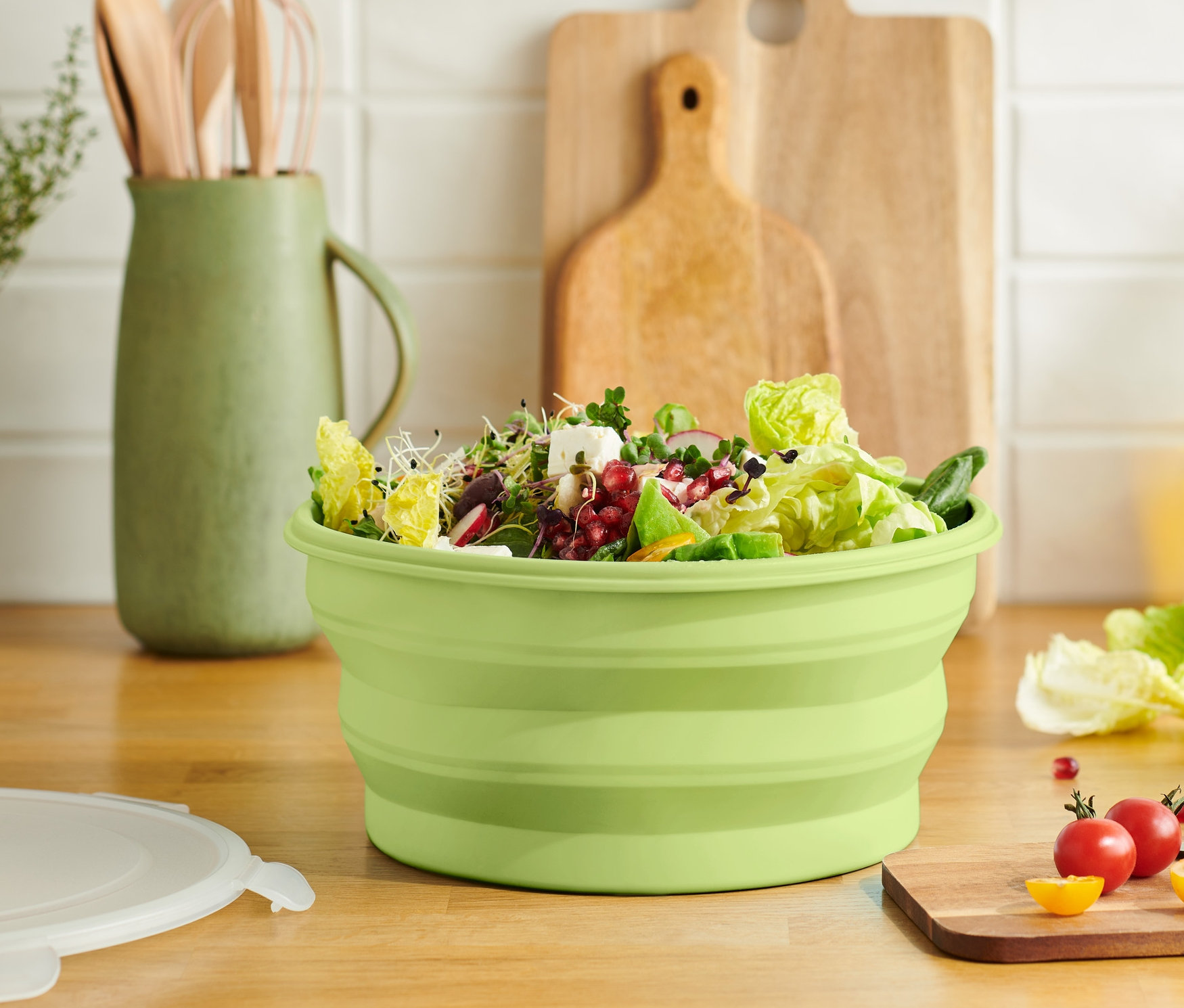 Grüne faltbare Salatschüssel gefüllt mit Salat auf einem Holzbrett.