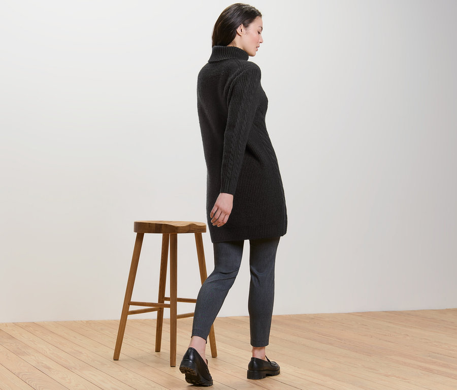 Frau von hinten trägt einen langen schwarzen Strickpullover mit Zopfmuster.