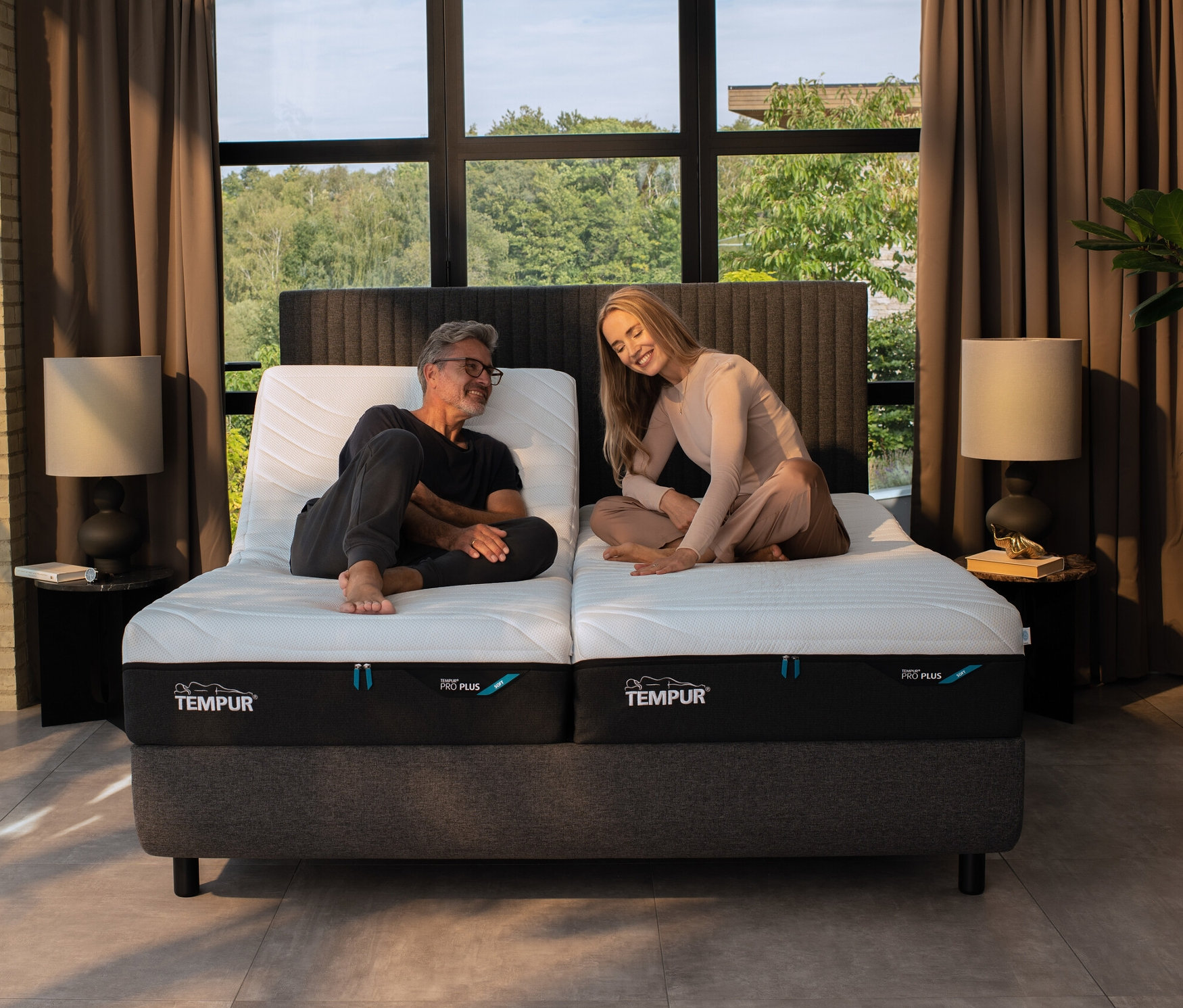 Ein Mann und eine Frau sitzen auf einem Bett mit TEMPUR® Systemrahmen elektrisch verstellbarer Lattenrost »Premium Flex 2000«.