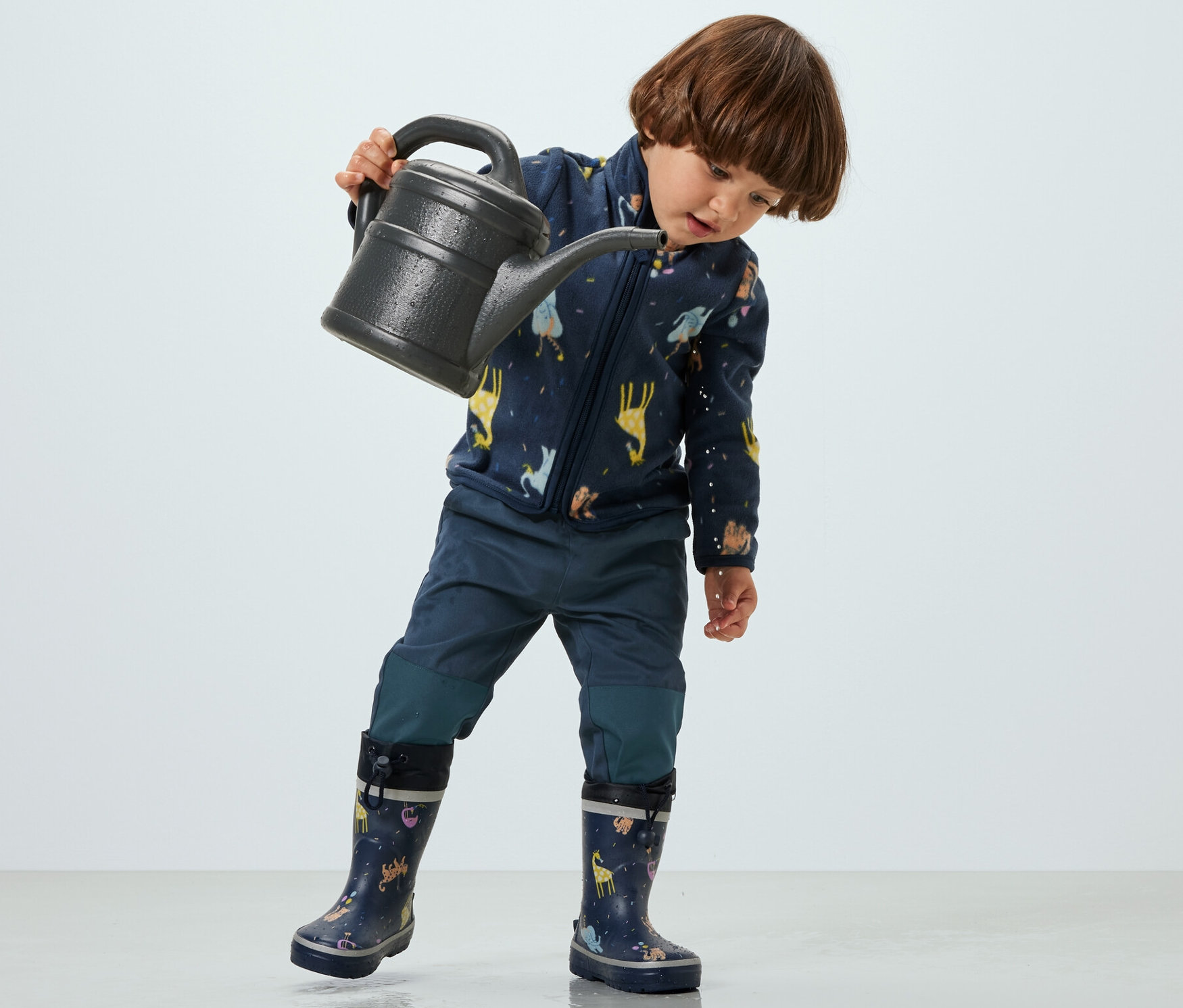 Ein Kind hält eine Gießkanne und trägt eine Kinder-Outdoorhose.