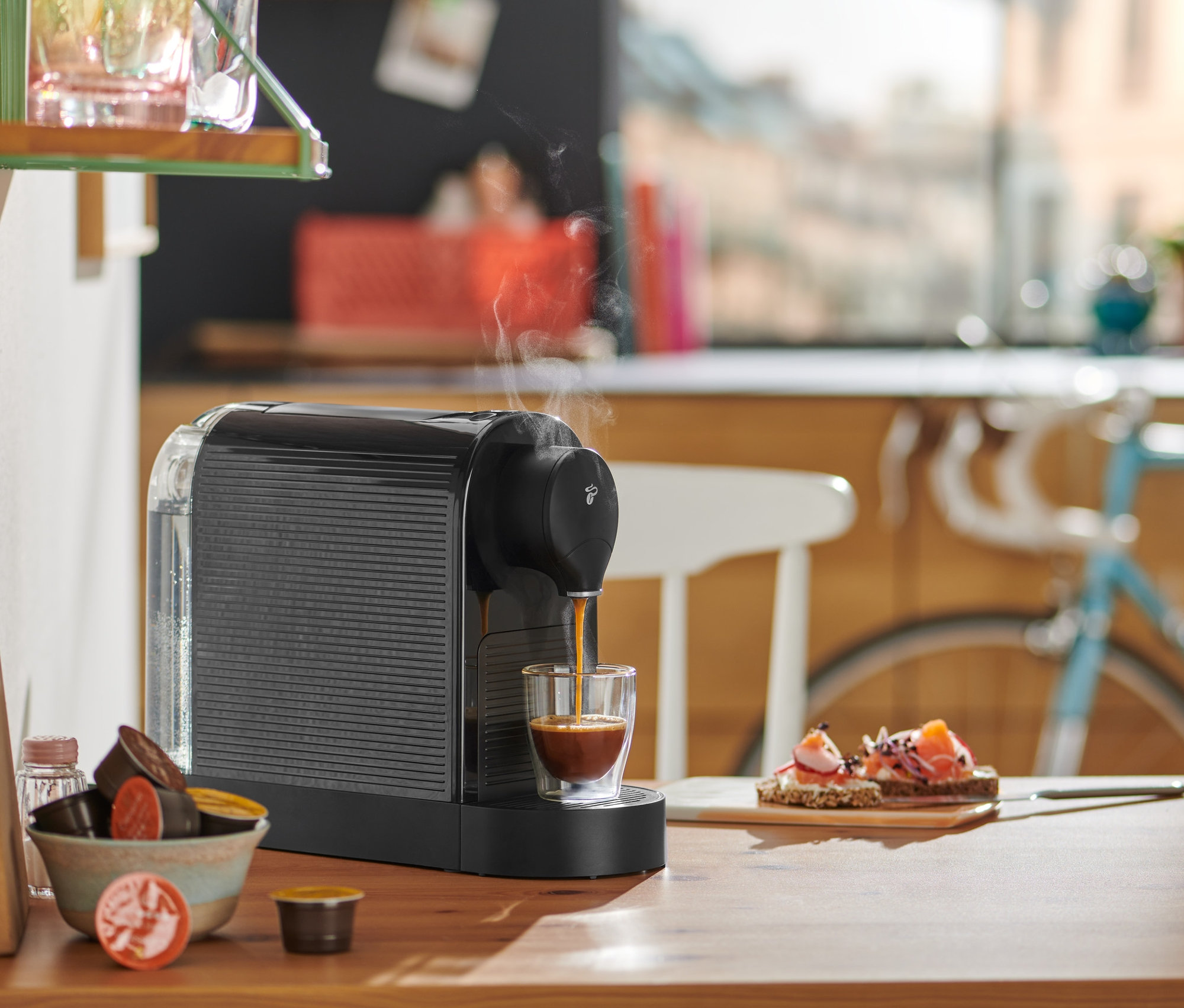 Schwarze Cafissimo pure+ bereitet Espresso in ein Glas auf einem Holztisch zu.