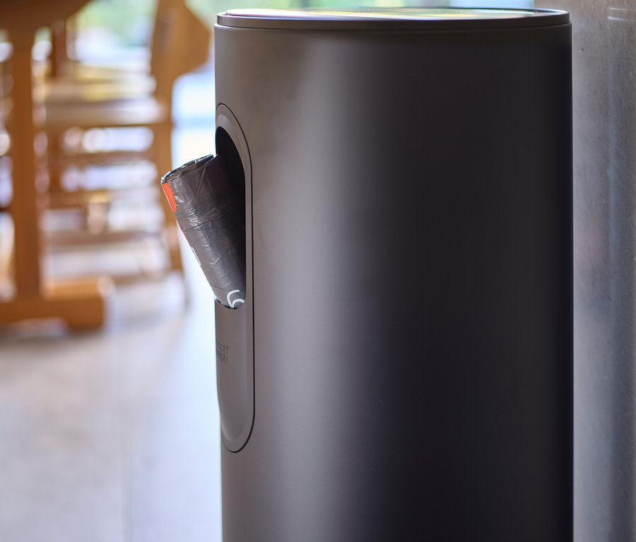 Ein schwarzer Abfalleimer mit einem schwarzen Müllbeutel, der aus einer Öffnung ragt.