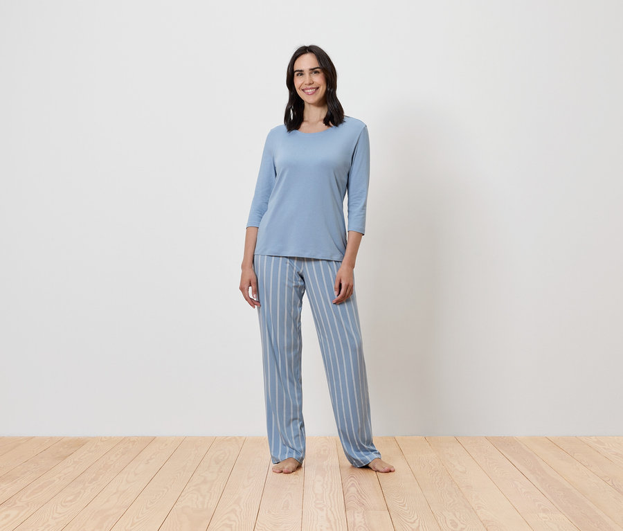 Frau steht und trägt einen blauen, gestreiften Pyjama.