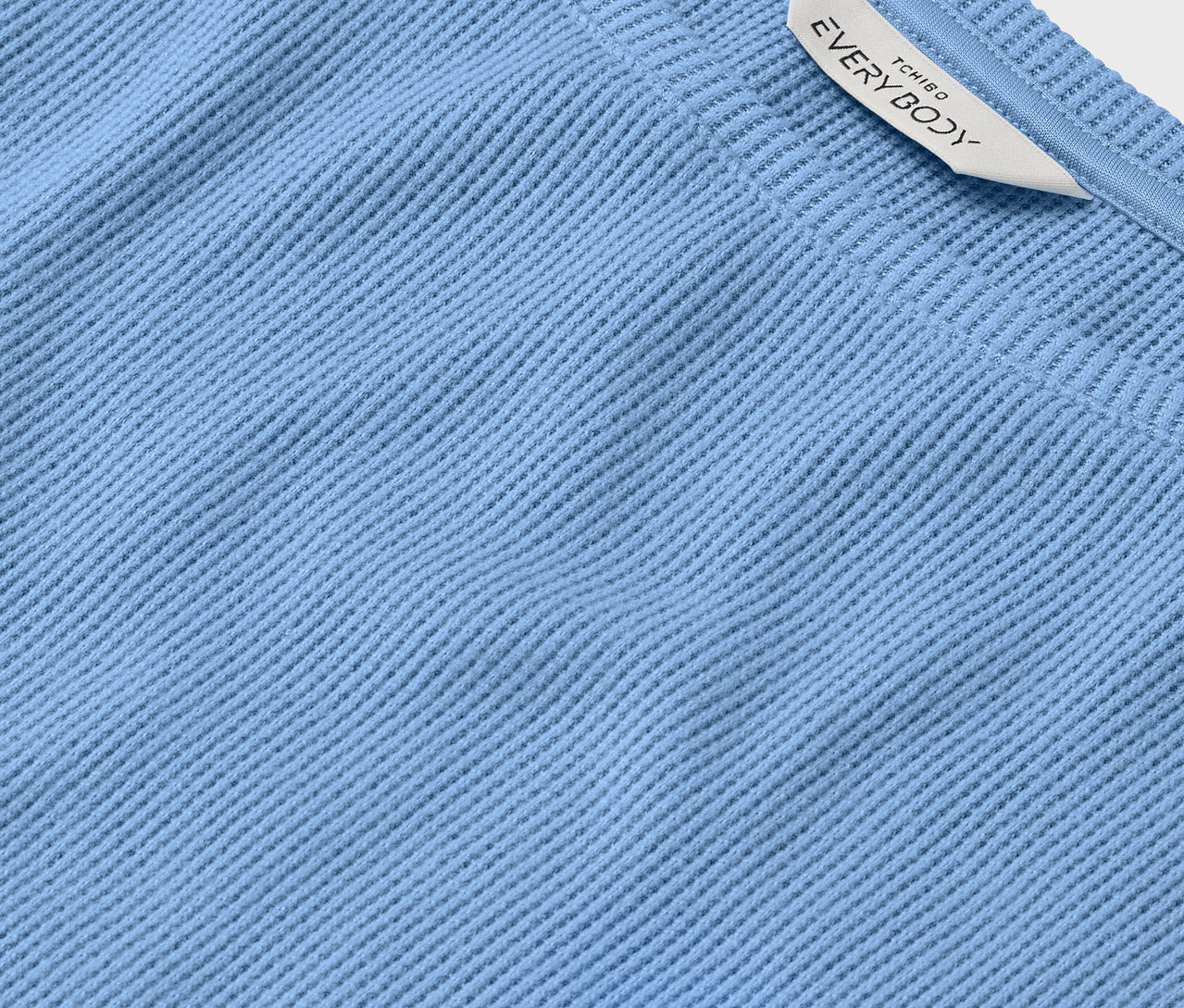 Detailaufnahme eines hellblauen Stoffes mit Rippstruktur und einem weißen Etikett mit der Aufschrift EVERYBODY.