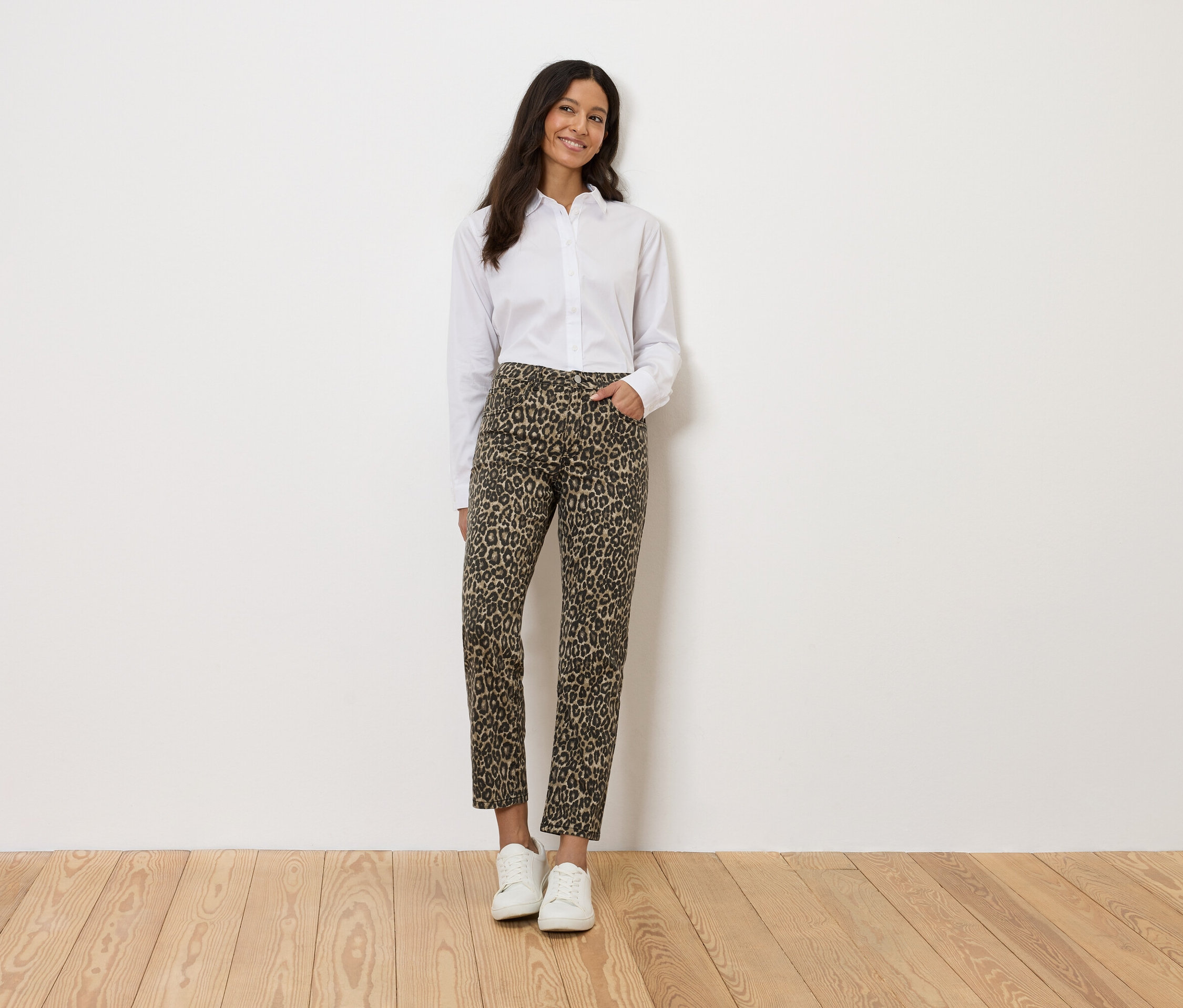 Frau in weißem Hemd und Leopardenhose, stehend vor einer weißen Wand.