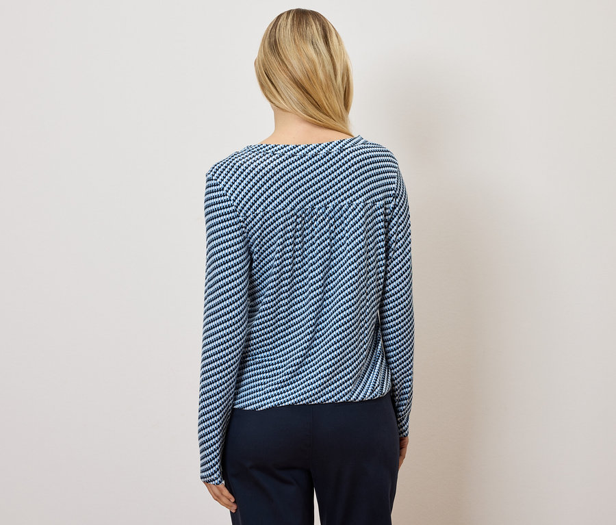 Rückansicht einer Frau mit blonden Haaren, die ein blau-weiß gestreiftes Oberteil und eine dunkelblaue Hose trägt.