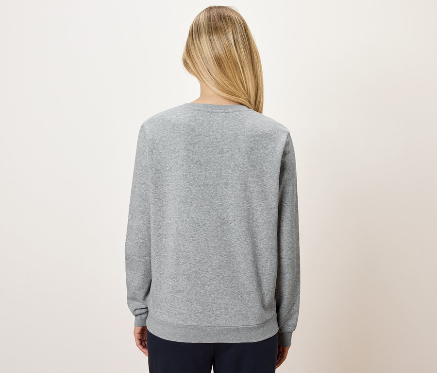 Rückansicht einer blonden Frau, die einen grauen Pullover und eine marineblaue Hose trägt.