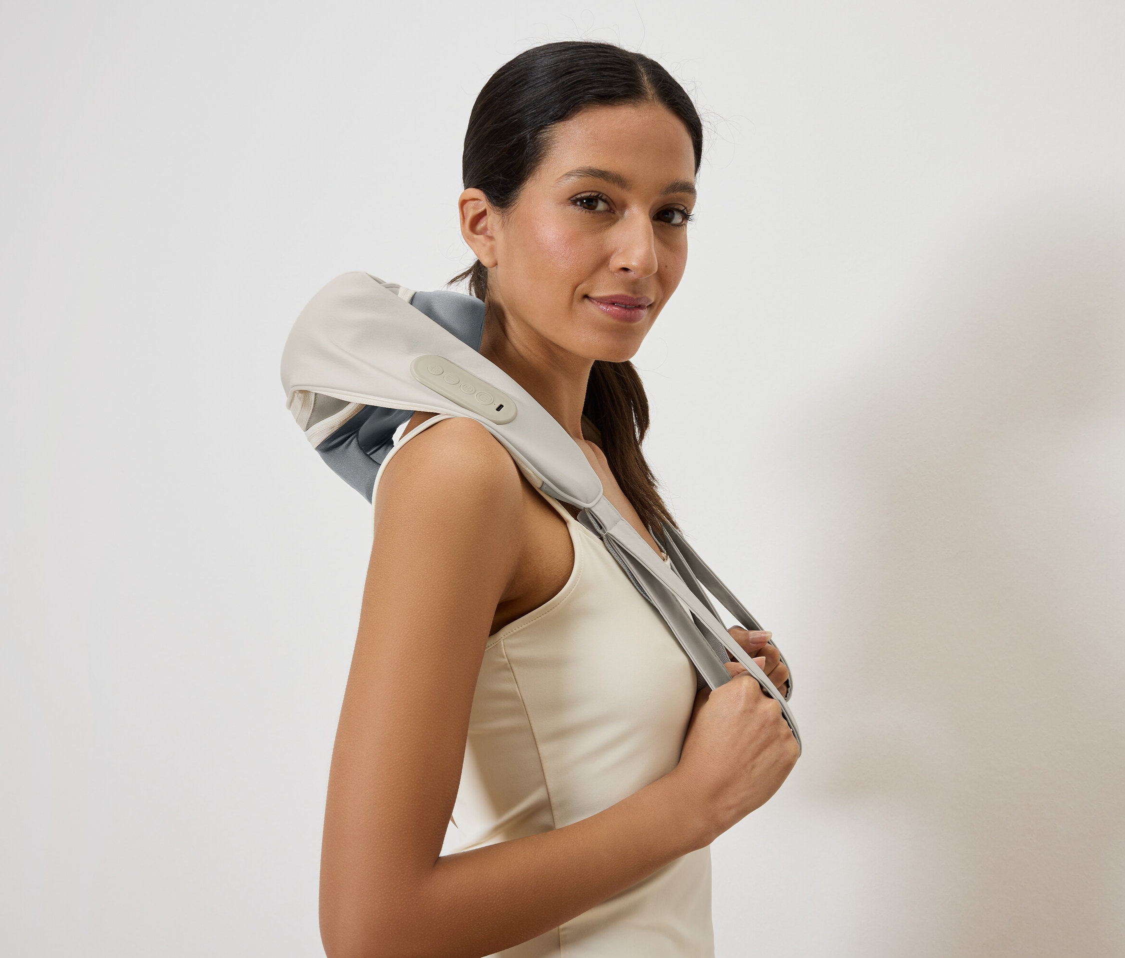 Frau mit einem Nackenmassagegerät in Grau und Beige über den Schultern, das Gerät wird mit den Händen gehalten.