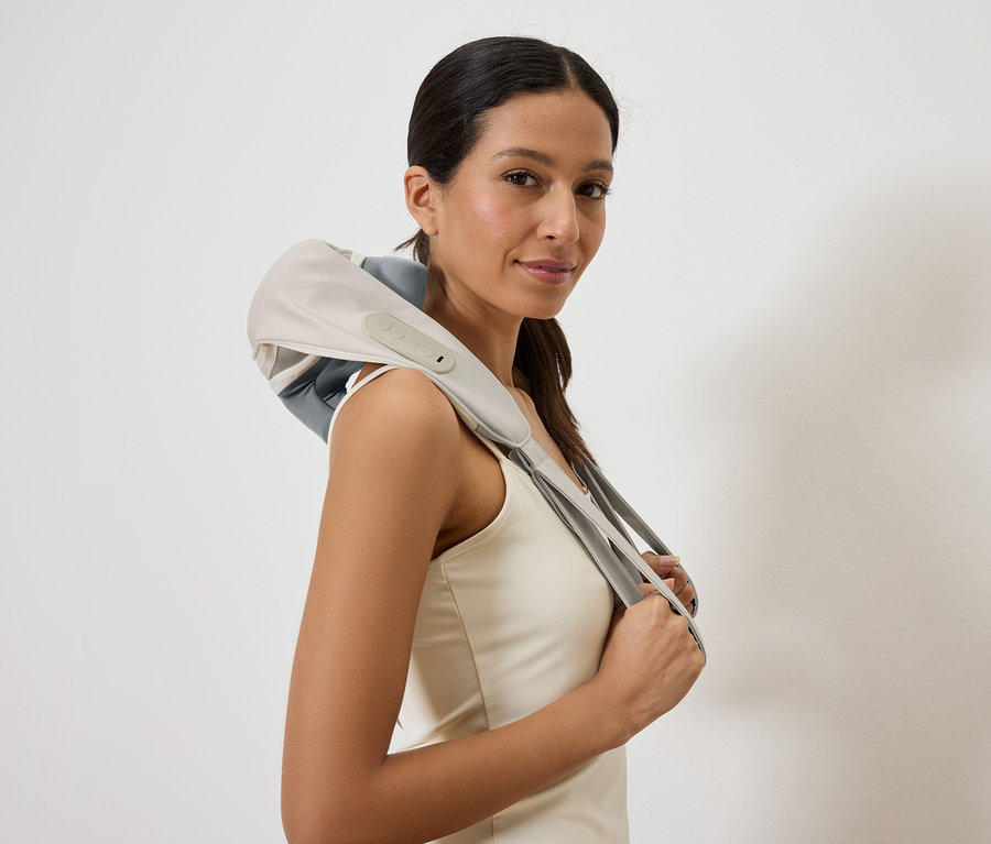 Frau mit einem Nackenmassagegerät in Grau und Beige über den Schultern, das Gerät wird mit den Händen gehalten.