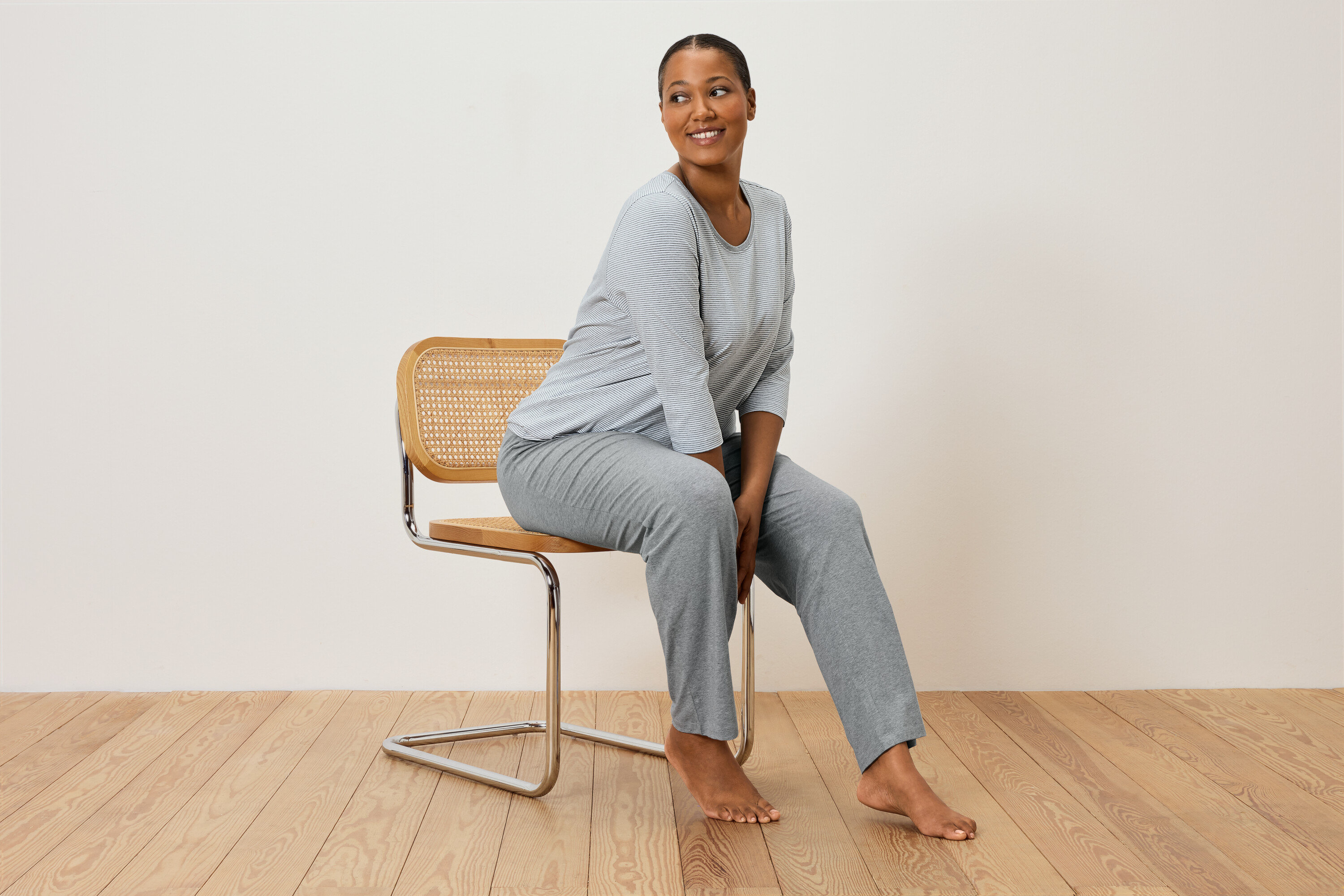 Frau sitzt auf einem Stuhl und trägt einen grau-weiß gestreiften Pyjama.